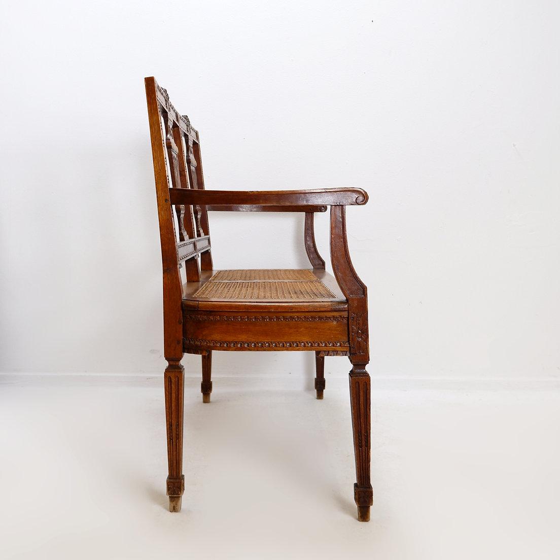 Banc de style néoclassique sculpté avec lyres sur le dossier du siège - 20e
Antiquité - Décoration - 20e
Dimensions : 101x 47cm H:95 SH:45cm 
Materiaux : Bois - Canne
Usure correspondant à l'âge et à l'usage.