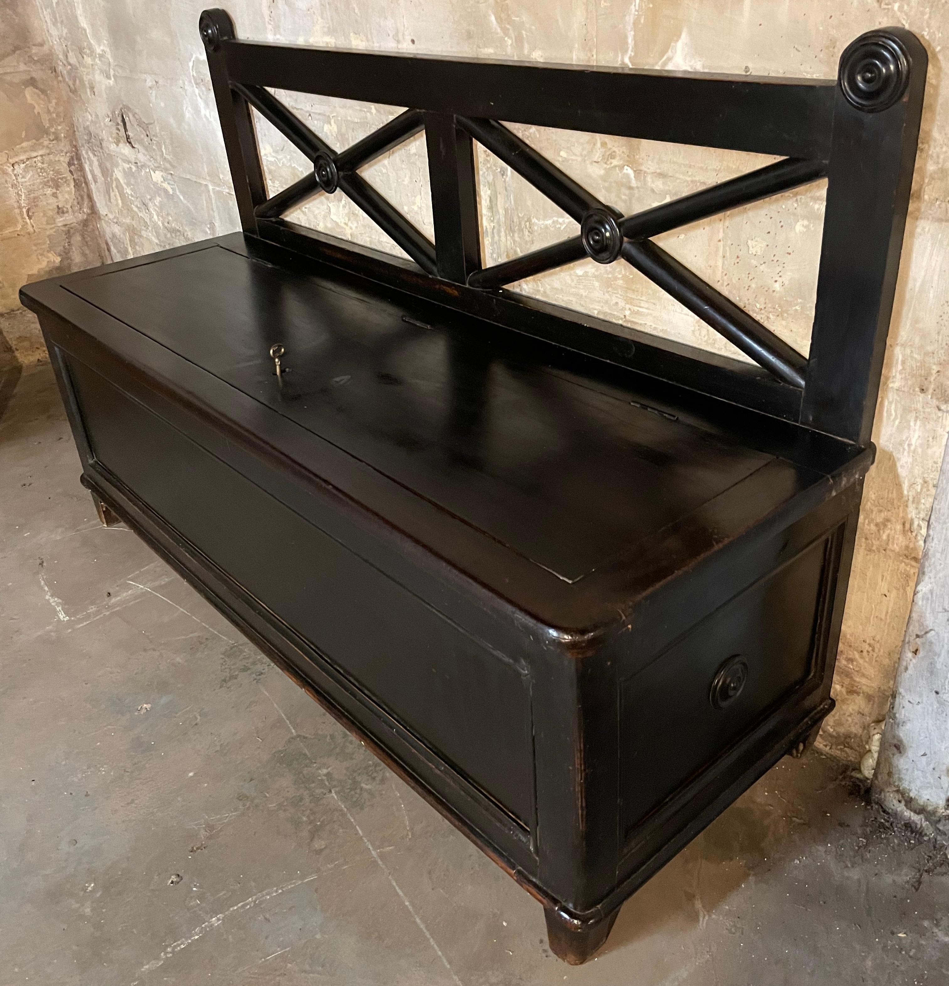 Neoclassical style bench. Severely handsome provincial neoclassical style dark stained wood bench with open double ‘X’ form back and circular metopes terminals at back and sides above long bench with keyed lock storage’s compartment for interior