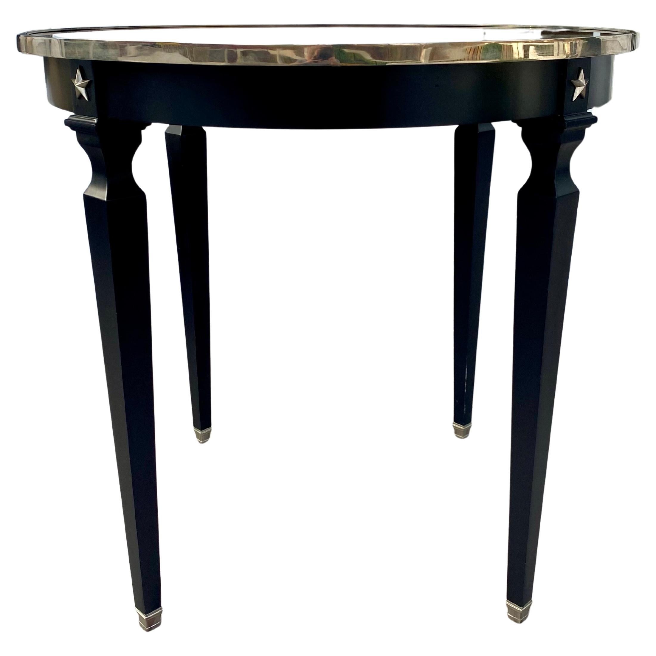 French Directoire style round center table by Global Views, Late 20th Century.  This tall matte black painted table features a reflective inset black glass top with polished silver trim, dimensional star embellishments, and decorative square sabots.