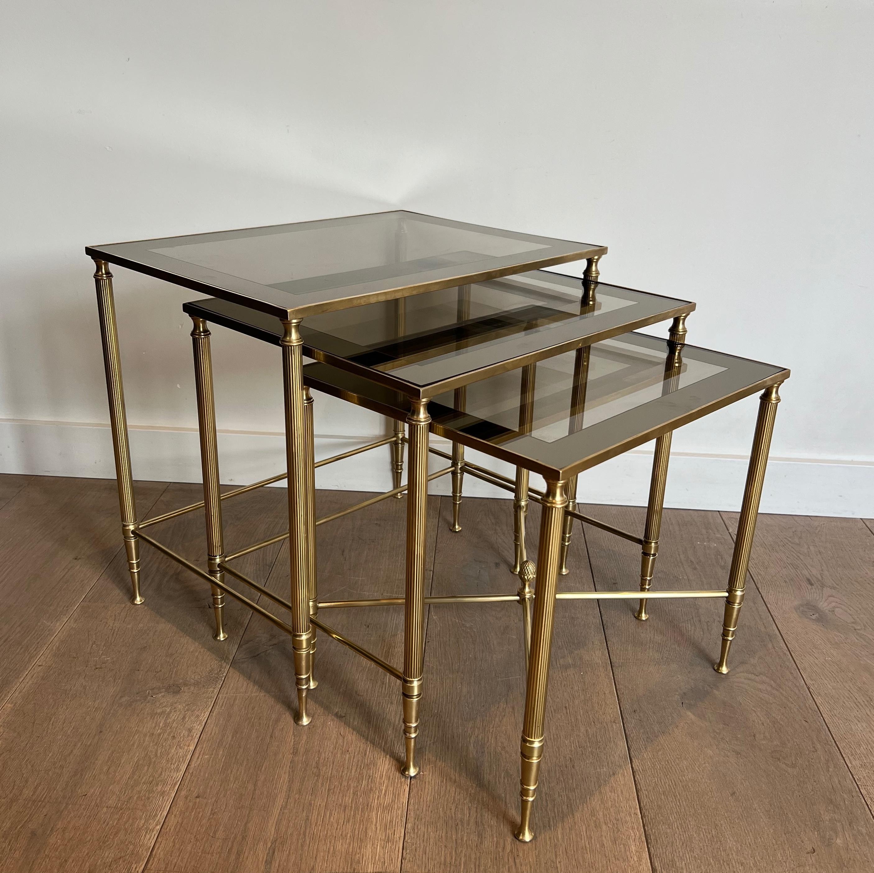 This set of three neoclassical style nesting tables is made of brass with glass shelves surrounded by a silvered mirror line . This is a French work by Maison Jansen. Circa 1940