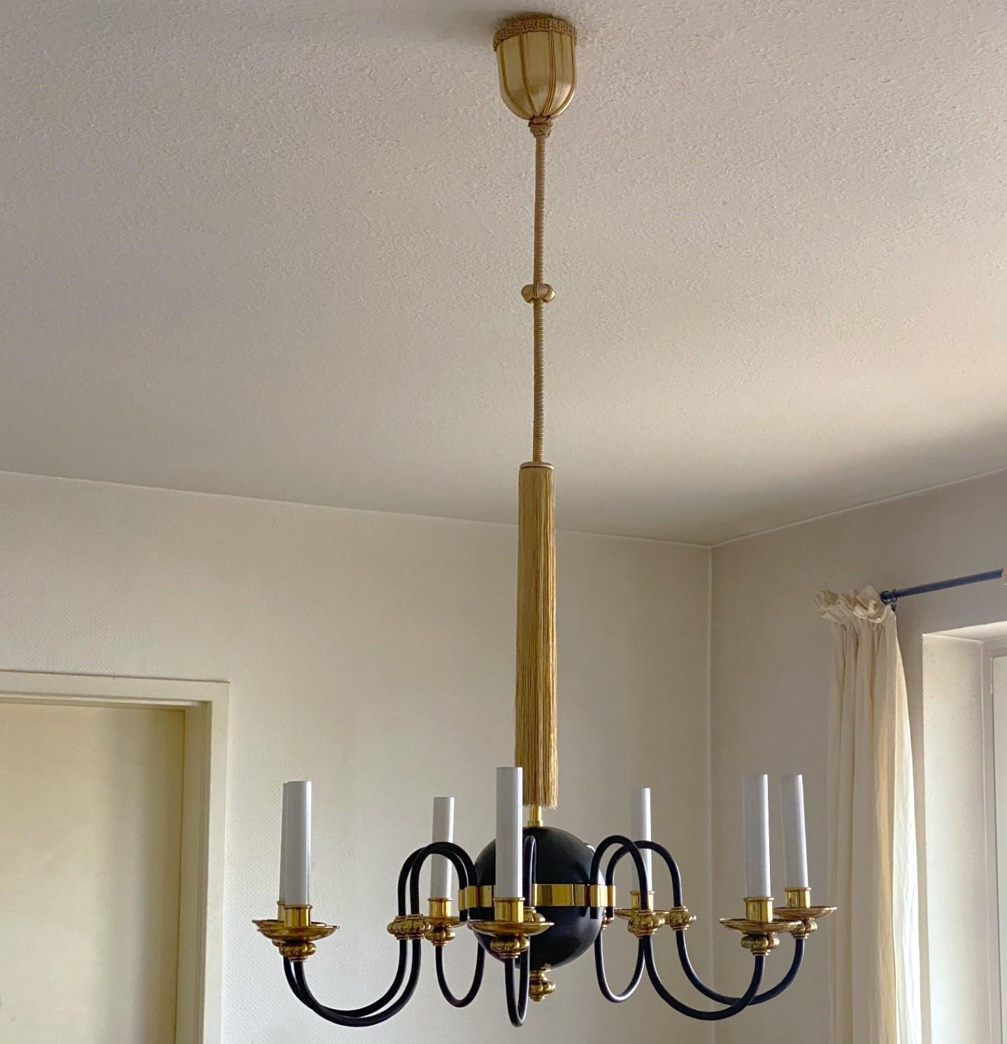 Eleganza e senza tempo: grande lampadario a sette luci in ottone dorato e annerito in stile neoclassico, Austria, anni Trenta. Sette bracci luminosi a volute con manicotti per candele sospesi a una corda di seta annodata a mano con una lunga frangia