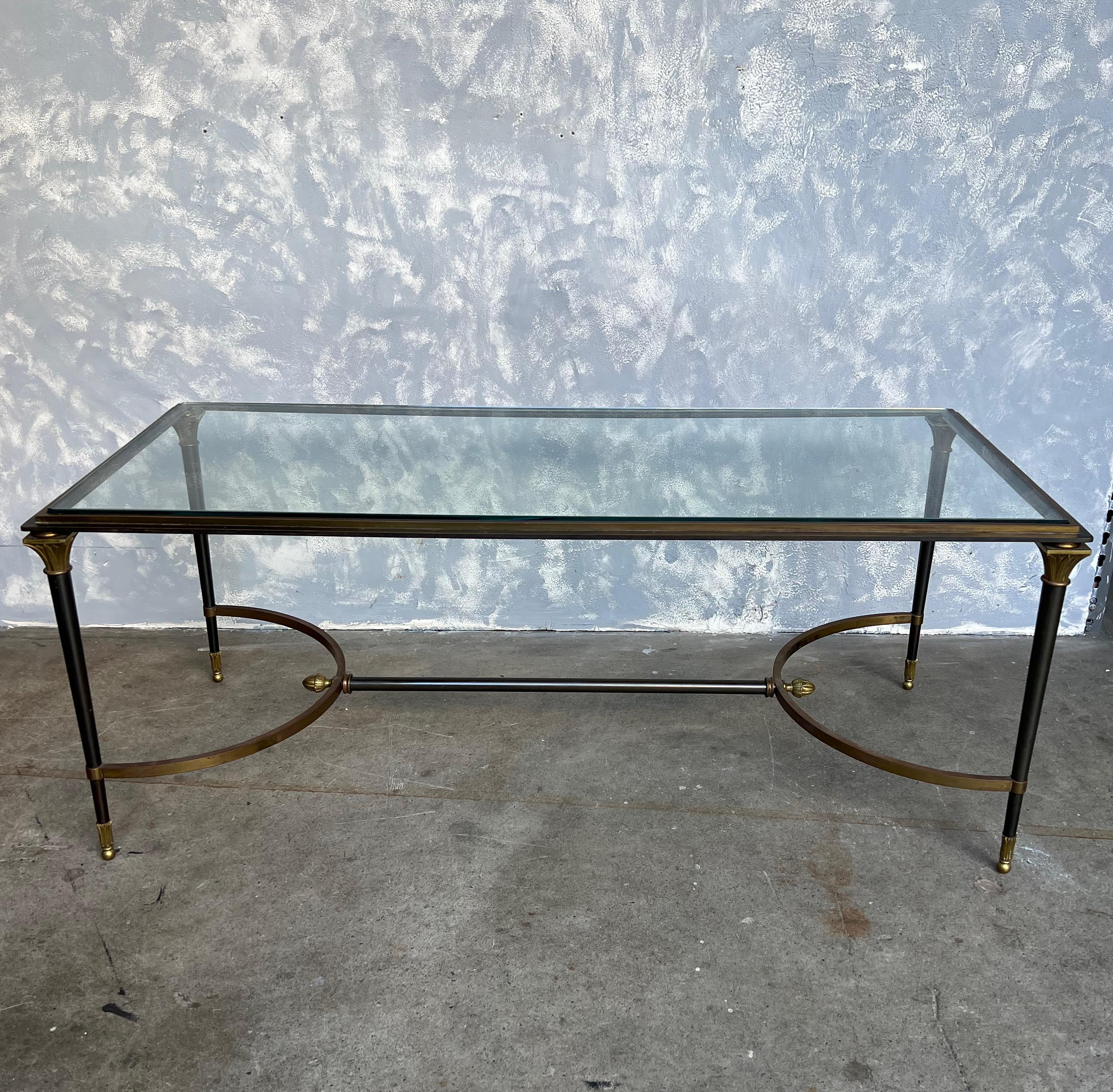 An elegant Italian 1960s Neoclassical style coffee table in the style of Jansen. The table is made of steel with classical gilt bronze decorative elements. The glass table top fits perfectly and the table is secured by a steel stretcher bar with