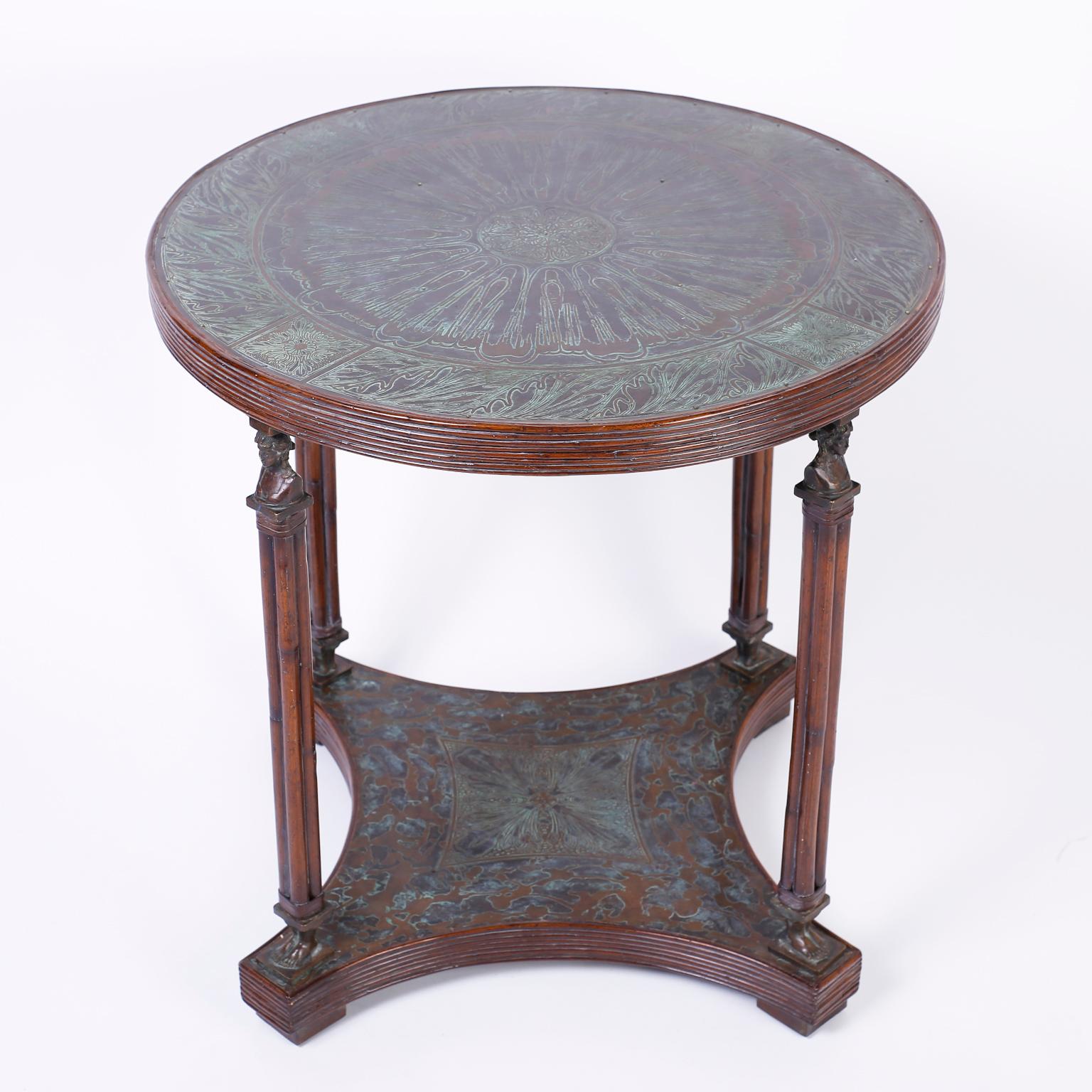 Midcentury center or occasional table with a round top clad in bronze over wood and decorated with three different patina techniques on hammered floral designs. The four columns have classical cast bronze figural heads and feet over a hammered