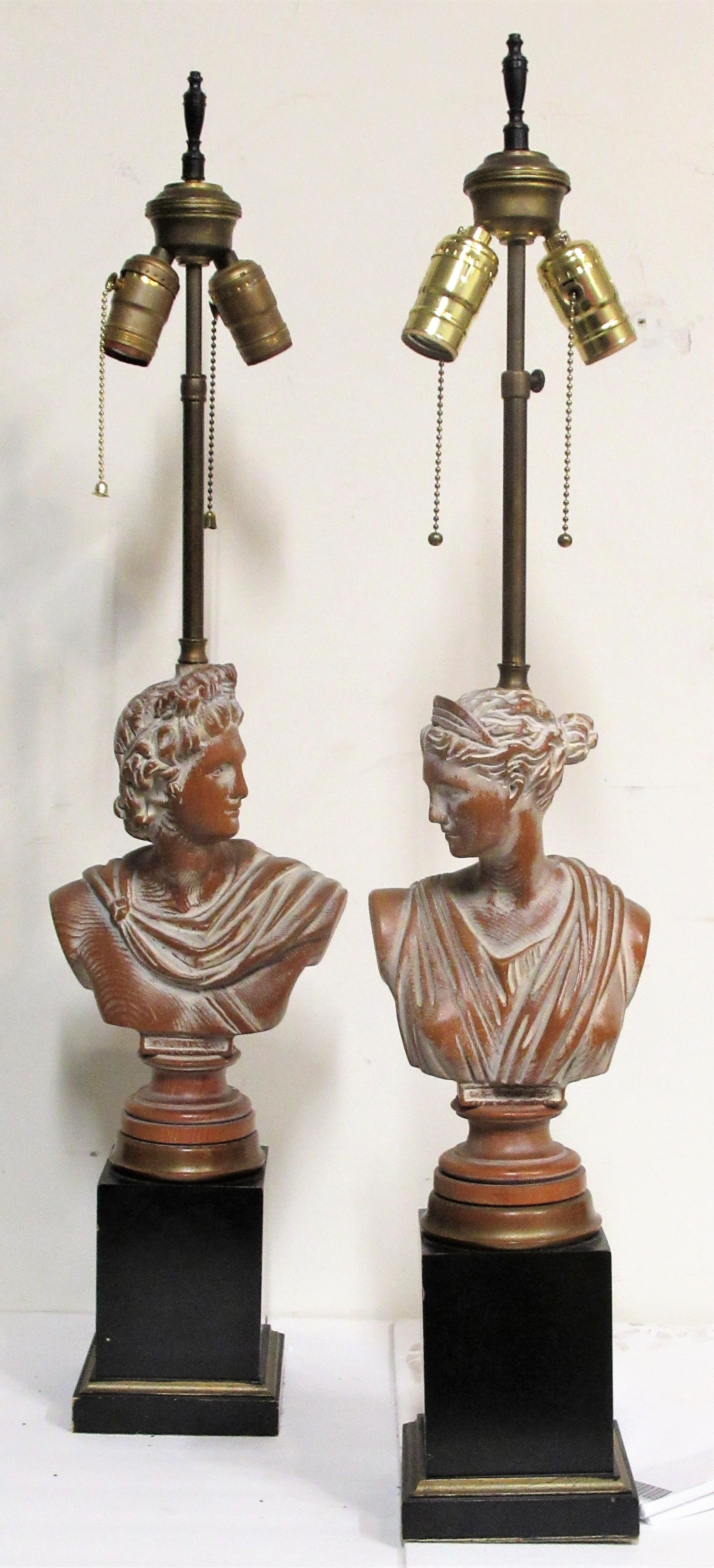 Pair of neoclassical antiquity style ebonized wood and brass trim pedestal base table lamps with original limed whitewashed and partially gilded surface to the carved wood busts of Daphne and Apollo, Circa 1940's-1950's. Look at all pictures and