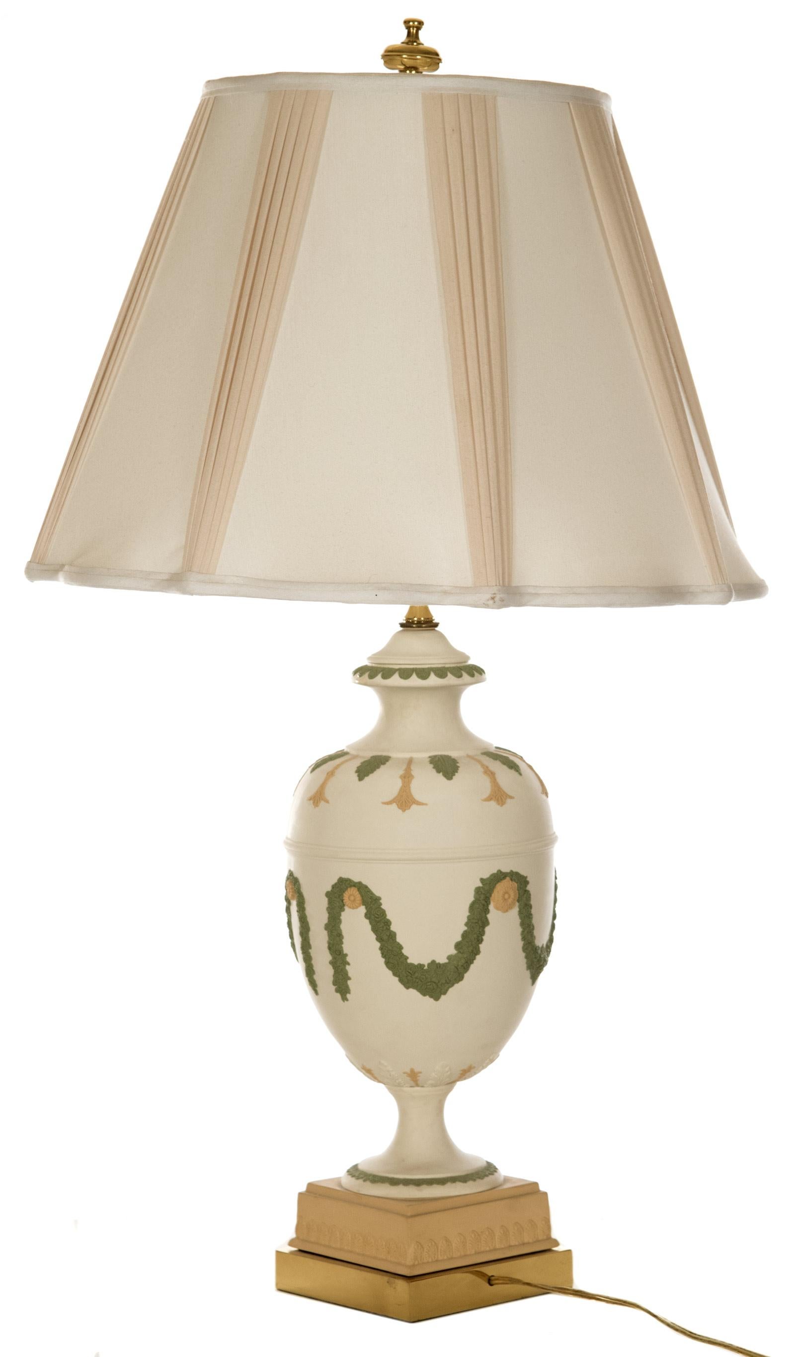 A neoclassical style ceramic table lamp of baluster form decorated with soft green and cream acanthus leaf motifs around the neck and shoulders of the form, the body with medallions supporting foliate garlands, raised on a square, cream plinth base,