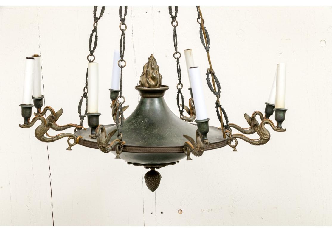 Lampadario d'epoca neoclassico a sei luci di forma tradizionale. L'urna piatta centrale con terminale a fiamma stilizzato e base con motivo a ghianda su un corpo in metallo con una raffinata patina verde. Le braccia sono creature alate del tipo