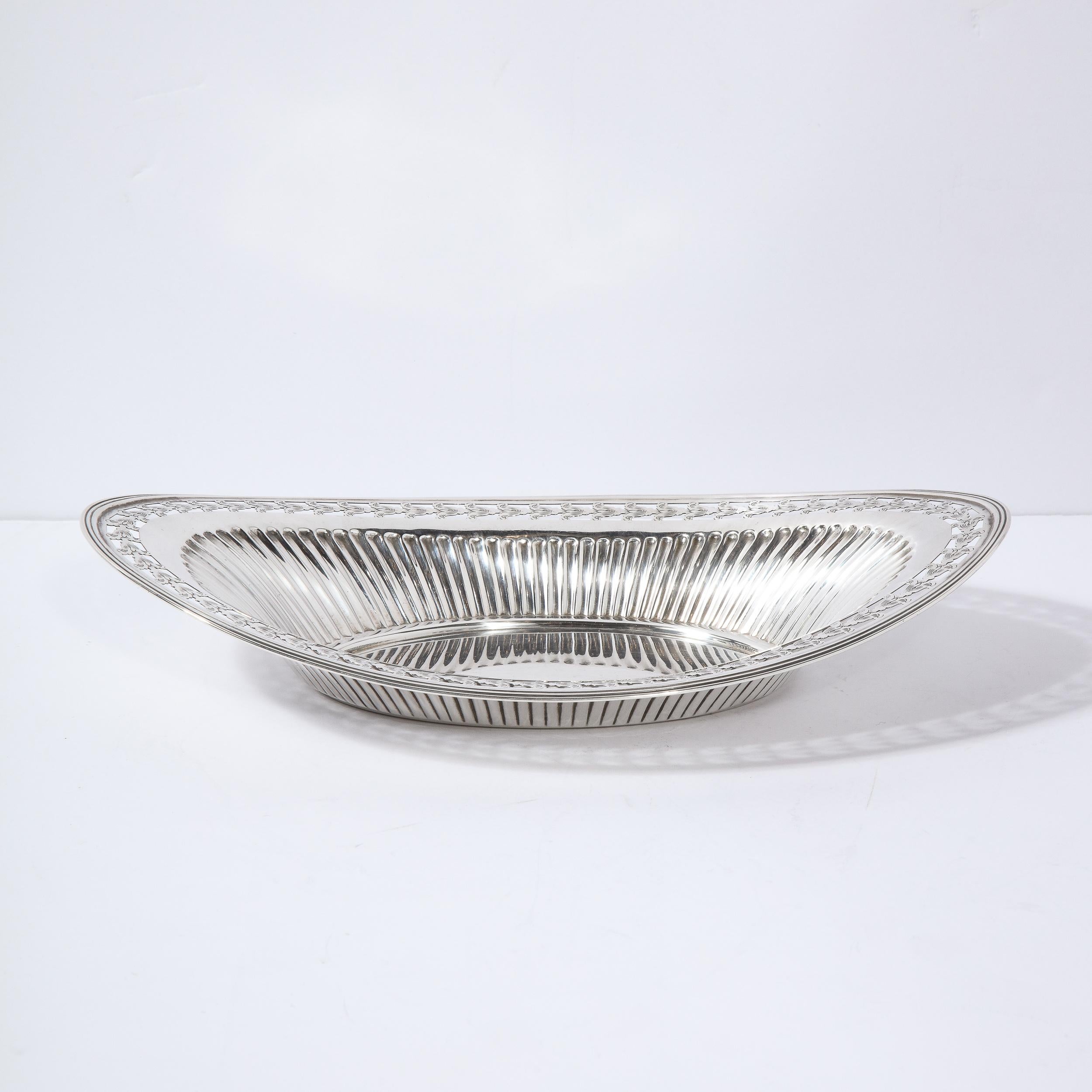 This refined neoclassical style tray features an oval base with undulating channeled sides and a banded exterior edge. Additionally, it offers recurring stylized acanthus leaf capitals (such as those which top corinthian columns) circumscribing the