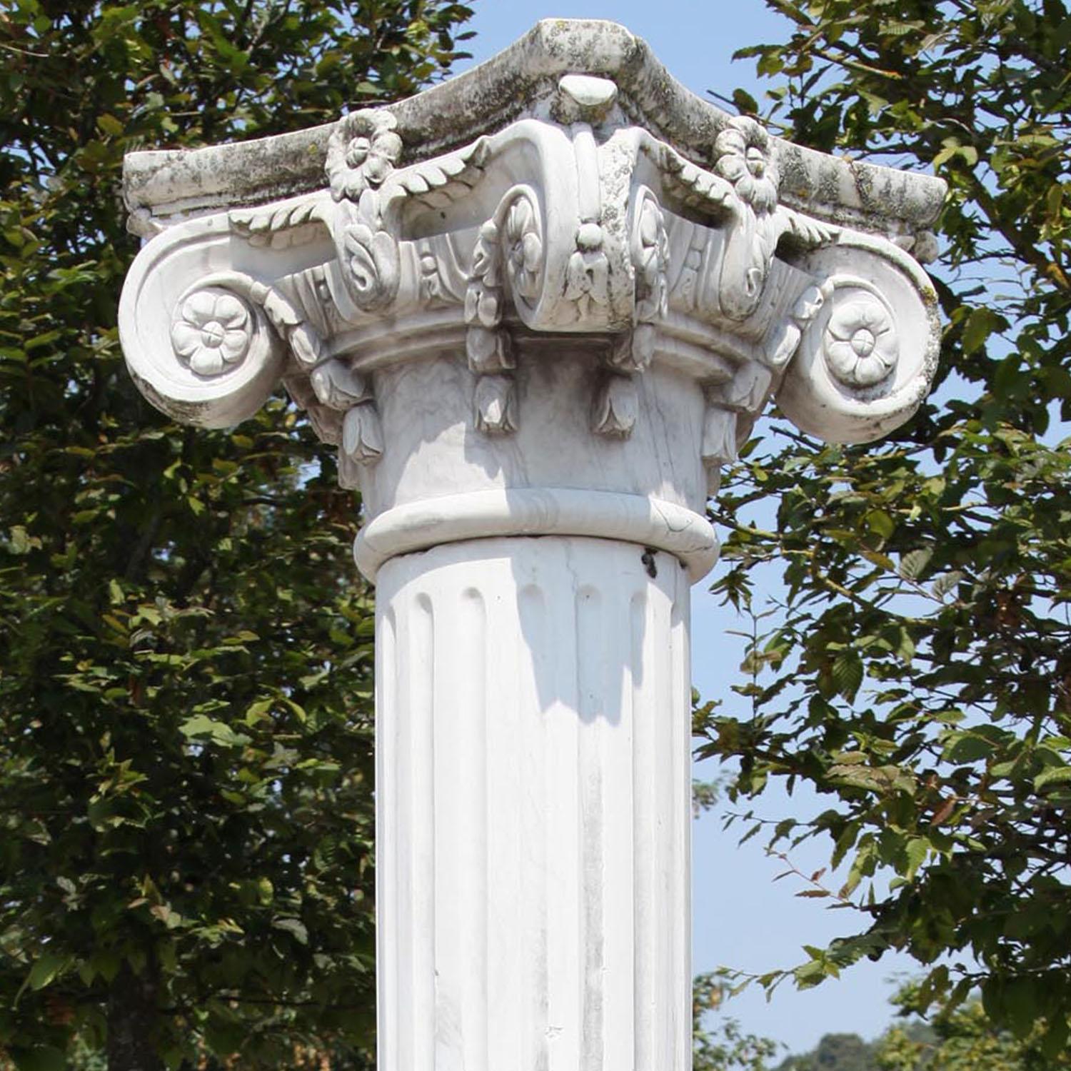 Tall column on a square plinth with a round base, a fluted shaft and a volute capita with flower décor. The column is hand-carved out of white marble.