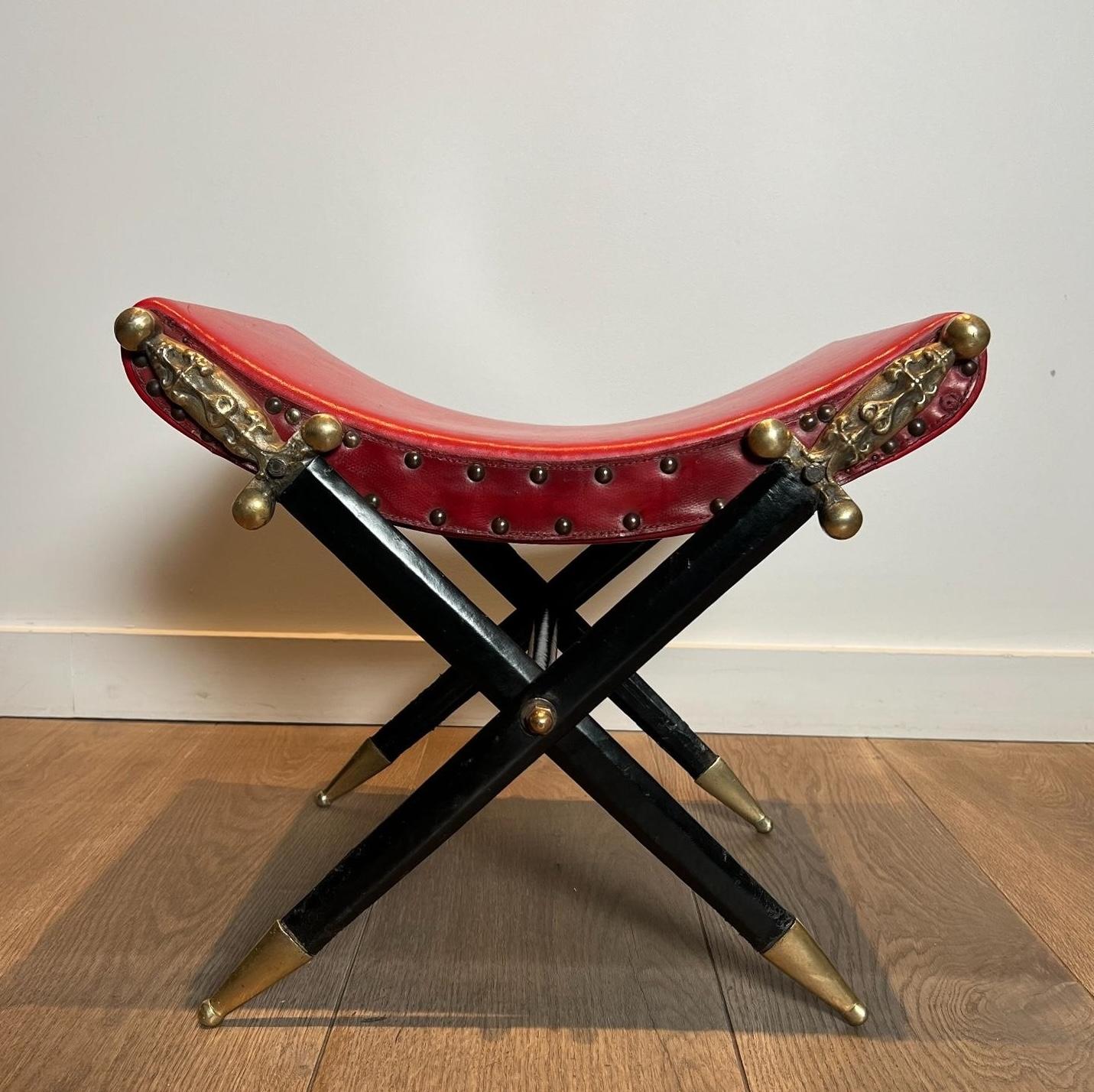 Ce très beau et intéressant tabouret Curule de style néoclassique est composé d'une assise garnie de cuir rouge, cloutée de laiton et reposant sur une base constituée d'épées croisées en bronze et métal recouvertes de cuir noir. Il s'agit d'un