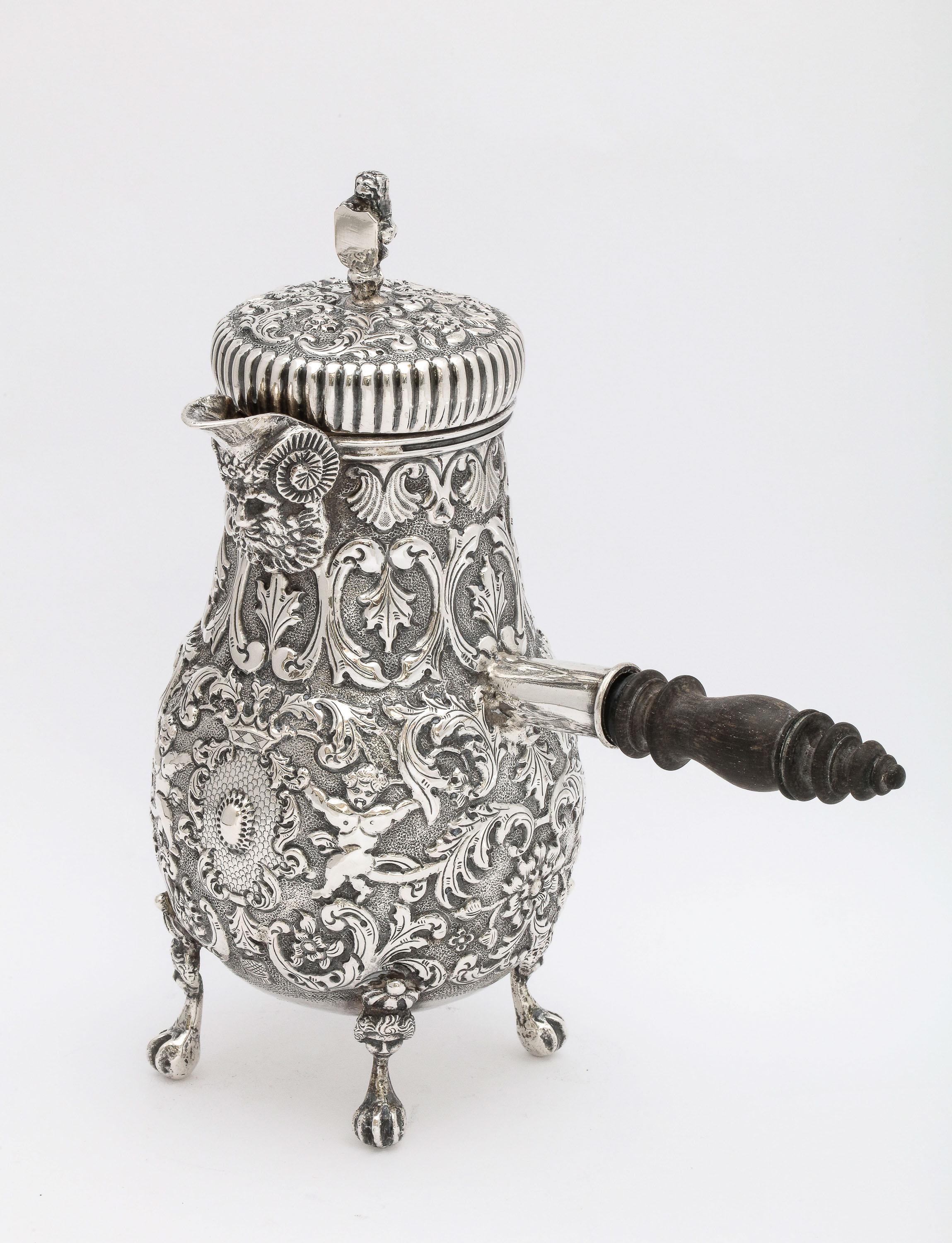 Chocolatera de estilo neoclásico, de plata continental (.800), con asa de madera y tapa abatible,  Holandés, con matrícula de 1886, Ate deGroot Boersma Sneek - fabricante. Hermoso y detallado diseño repujado (con querubines, hojas, etc.) y con la