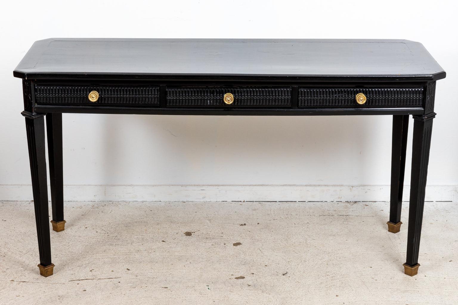 Circa late 20th century Neoclassical style ebonized writing table or console with brass accents on castors. The table is also constructed with three drawers and carved drawer fronts. Made in France. Please note of wear consistent with age including