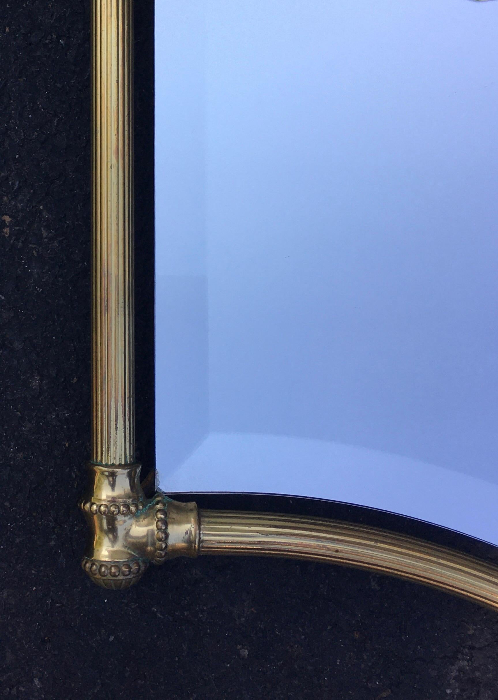 Handsome pair of neoclassical style gold brass wall mirrors. Beautifully patinated curved metal frames support floating beveled mirrors with fluted ribbed rods and beaded detailing. Pair would be beautiful displayed over a double bathroom vanity.