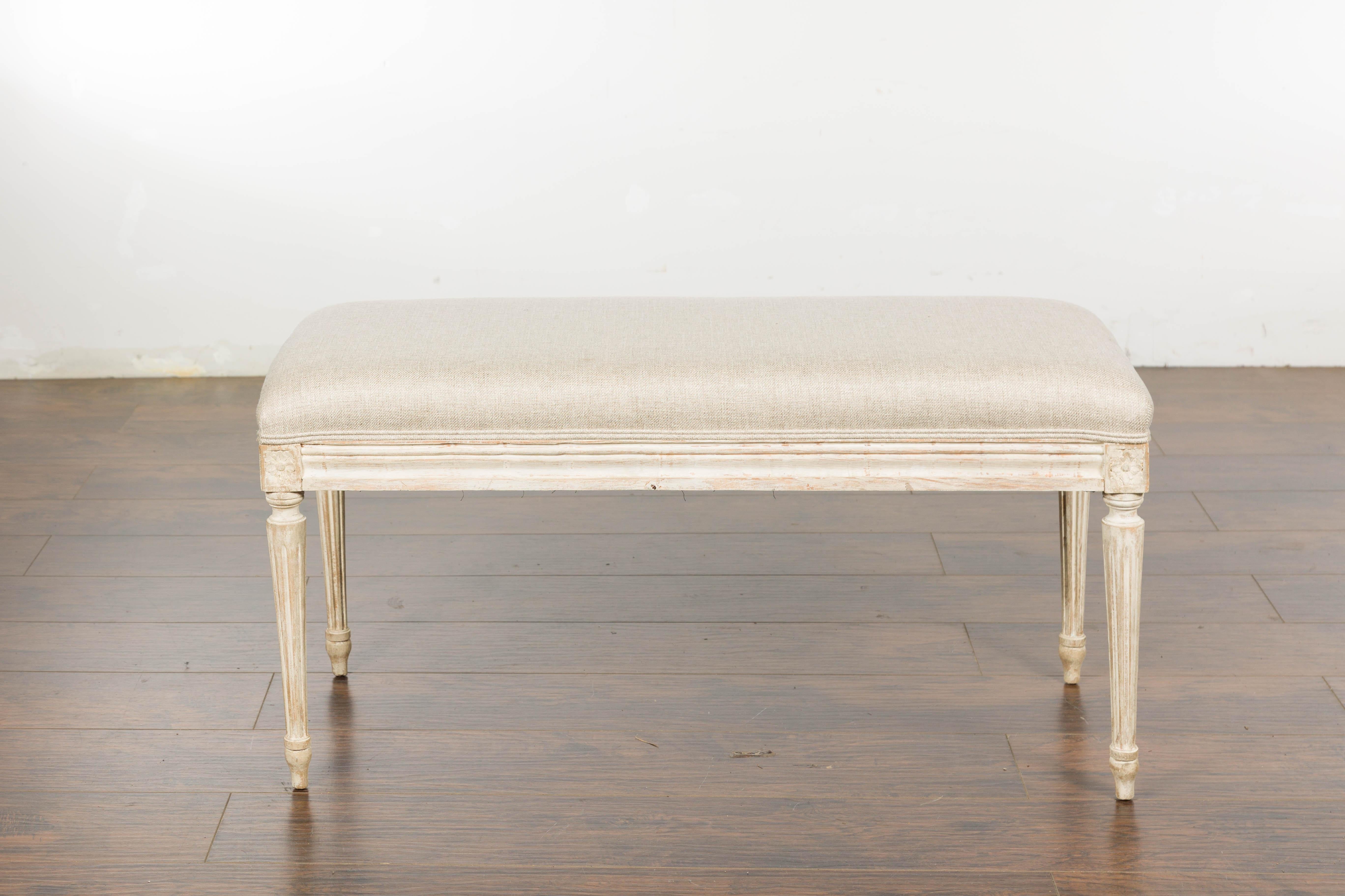 A French Neoclassical style painted walnut bench from circa 1900 with carved décor and new custom upholstered seat. Immerse yourself in a wave of elegance with this French Neoclassical style walnut bench from circa 1900. This beautifully designed