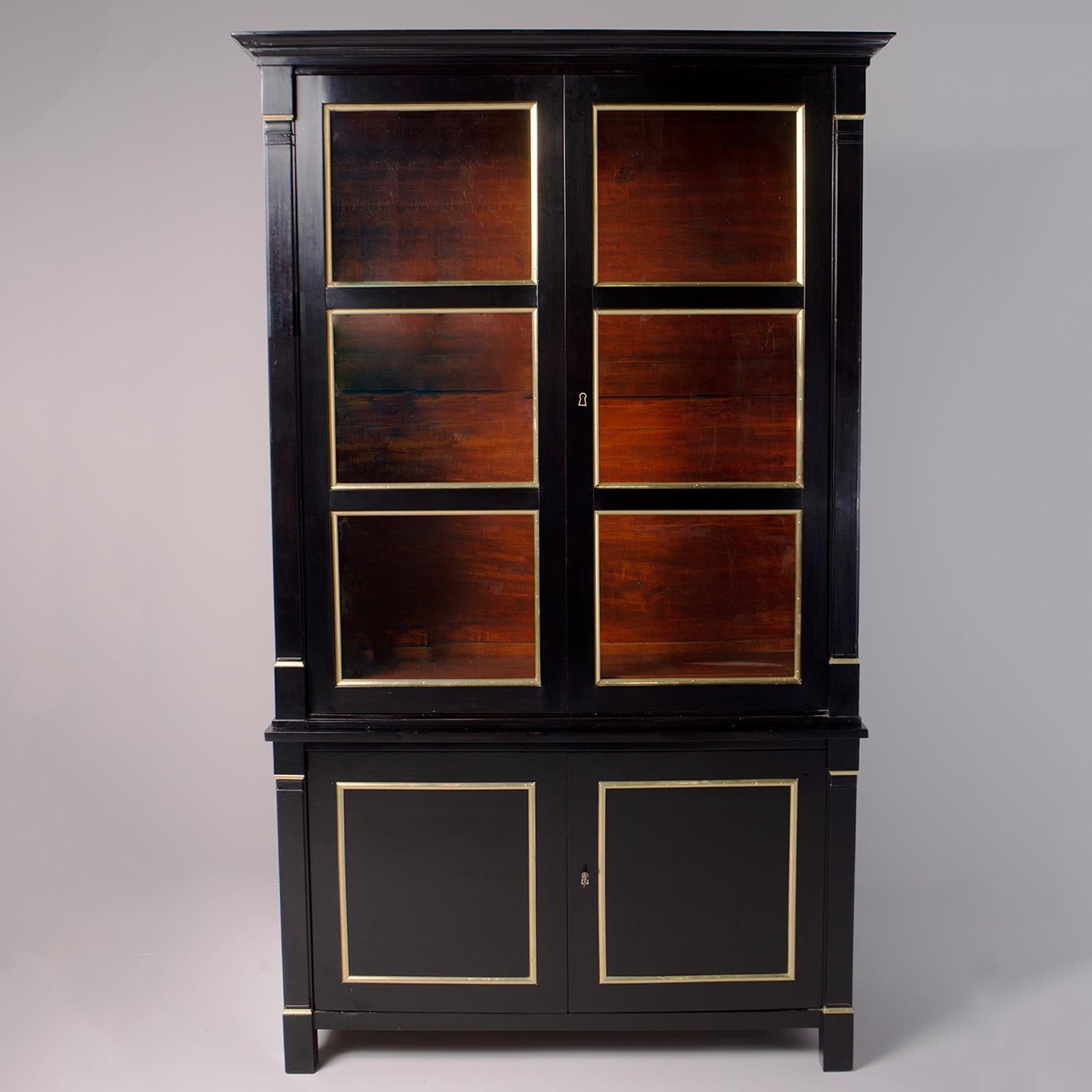Neoclassical French bookcase is newly ebonised and trimmed in brass, circa 1920s. Cabinet consists of two pieces that can be separated for moving and shipping. The bottom base has two hinged locking cabinet doors with single internal shelf. The top