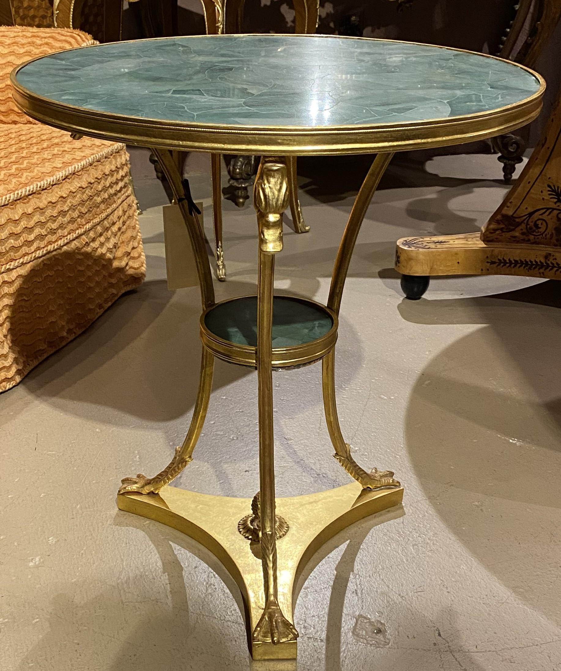Guéridon rond en bronze doré de style néoclassique, avec plateau en pierre verte et étagère médiane, orné de supports à tête de canard ou d'oie, les pieds de la table se terminant par des pattes d'oiseau, le tout rehaussé d'un fleuron central en