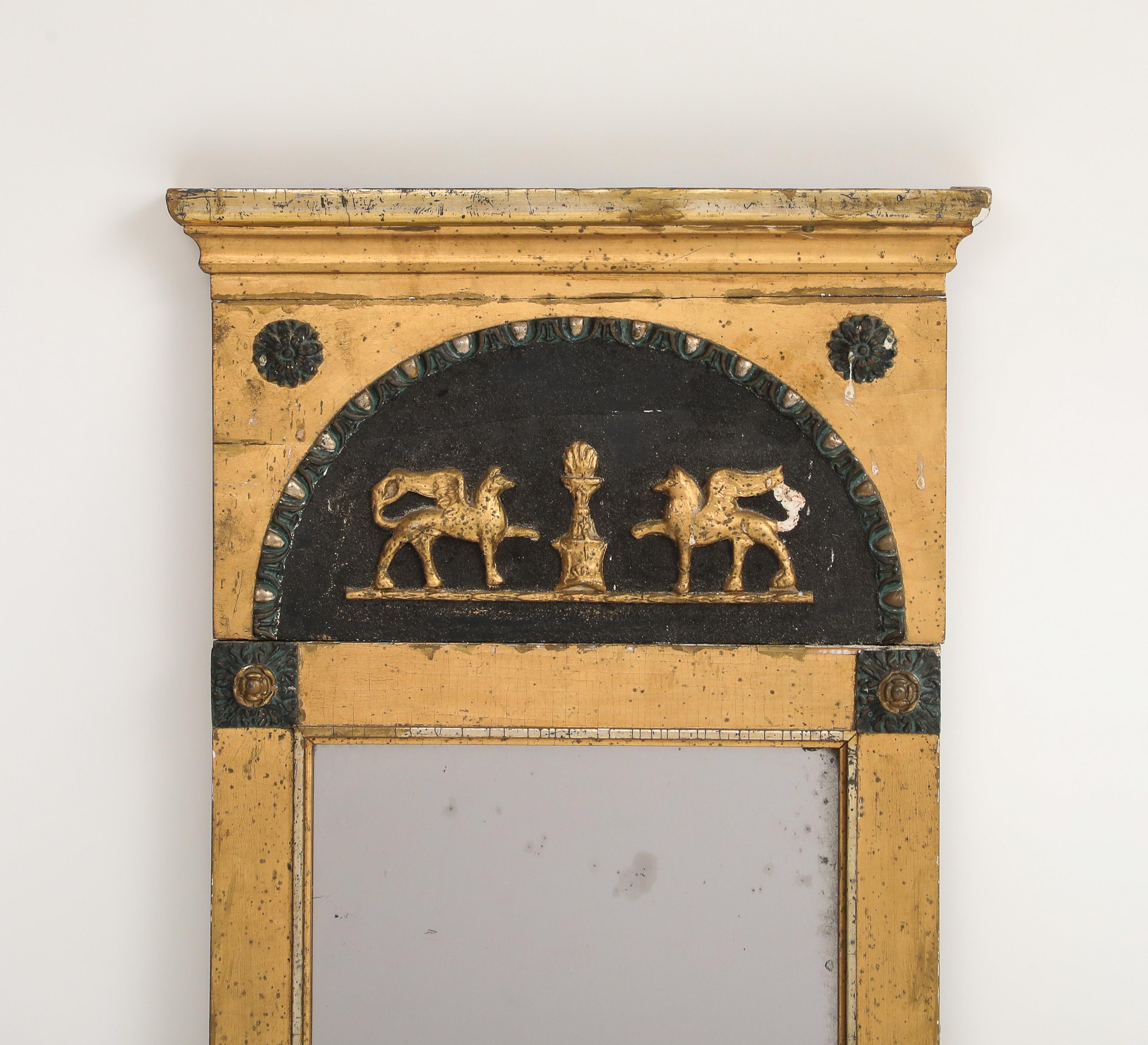 Espejo de pared de estilo neoclásico del siglo XIX con marco de madera dorada e intrincados elementos decorativos de bronce. La parte superior presenta motivos clásicos, incluidas dos figuras de caballo doradas que flanquean una urna central.