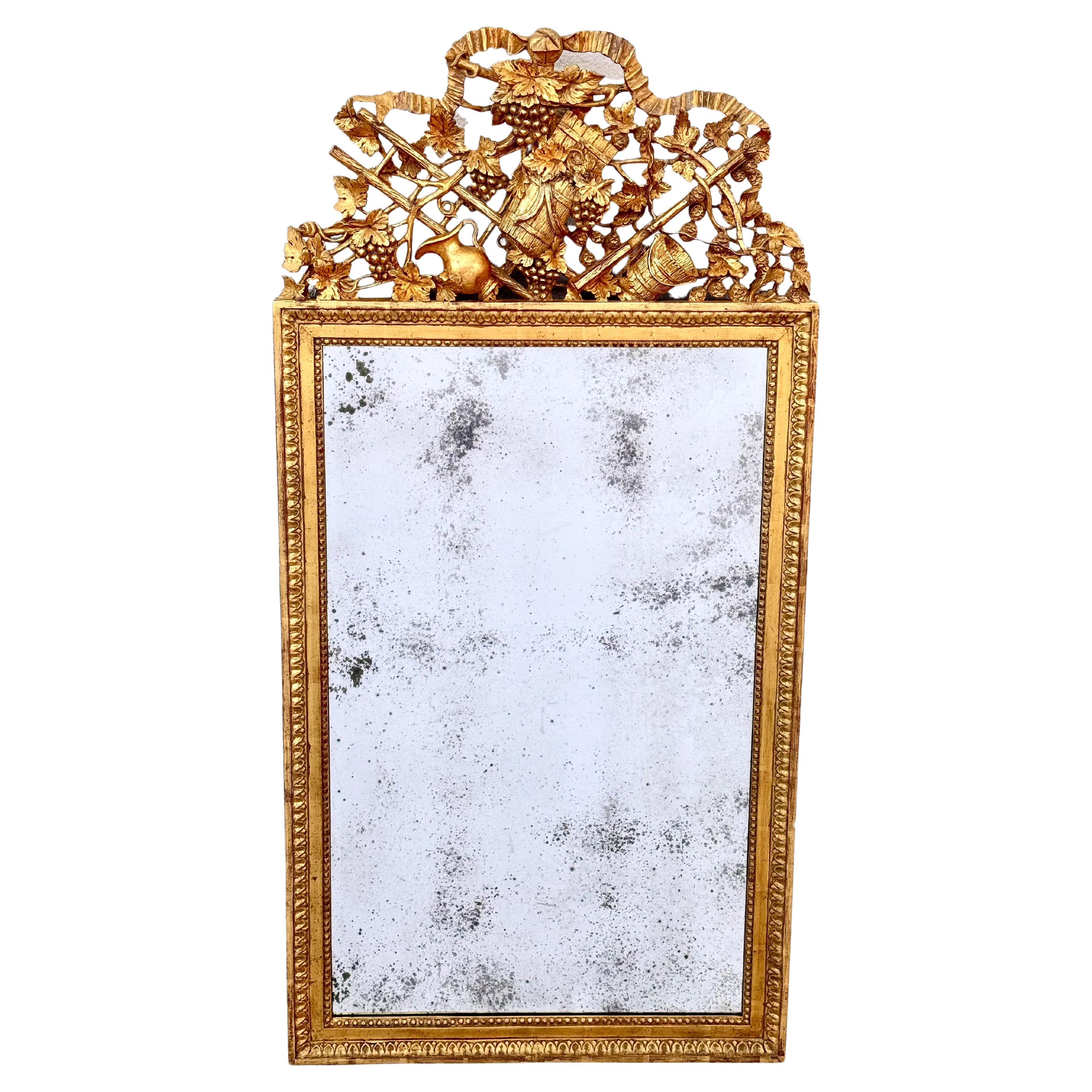 Neoclassical style giltwood and gesso mirror. 
The rectangular mirror plate within a leaf-tip carved surround, surmounted by an arched cresting carved with grape clusters and farm implements.  
