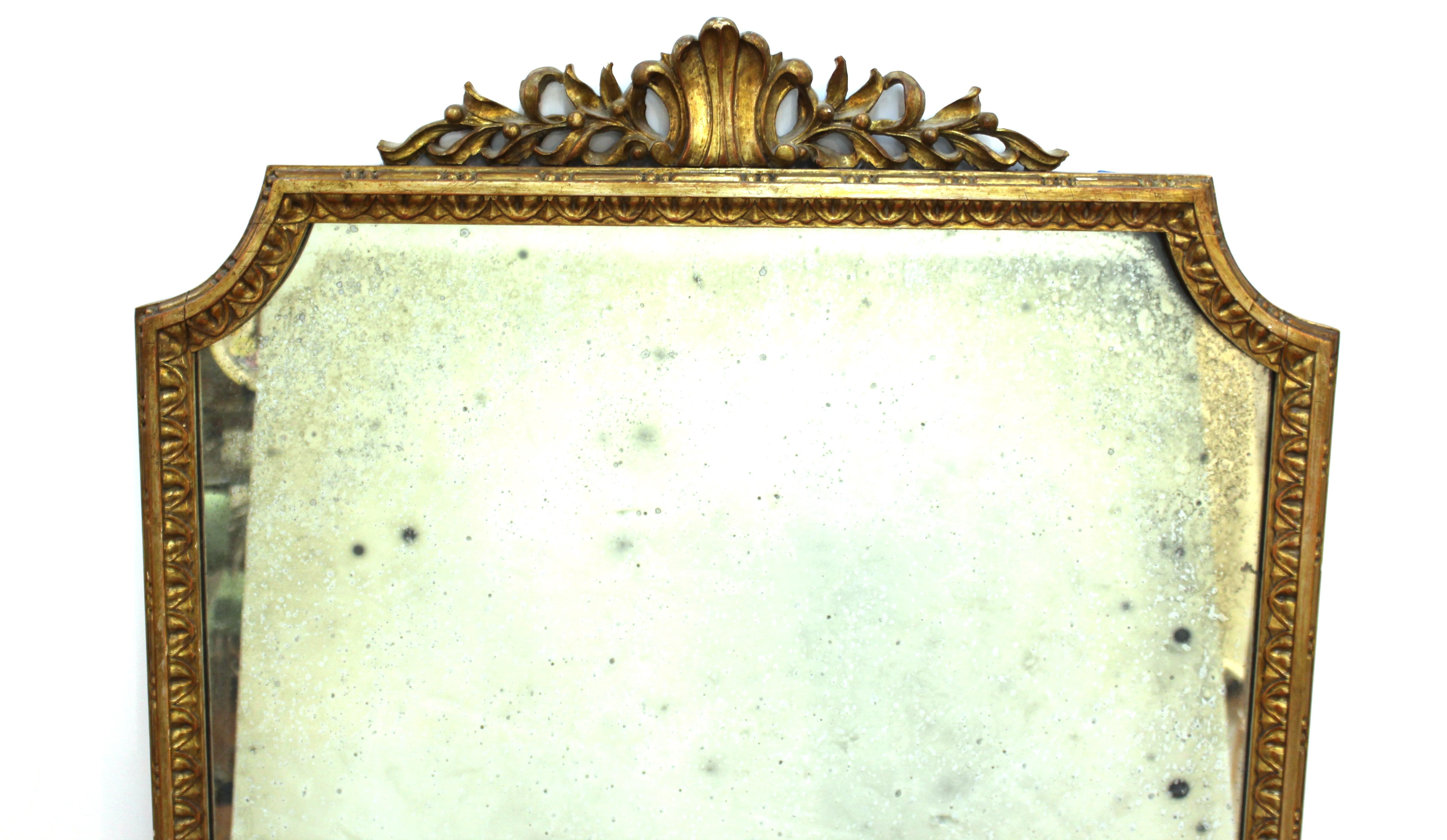 Miroir mural de style néoclassique avec cadre en bois doré sculpté et verre miroir vieilli. 

Concessionnaire : S138XX