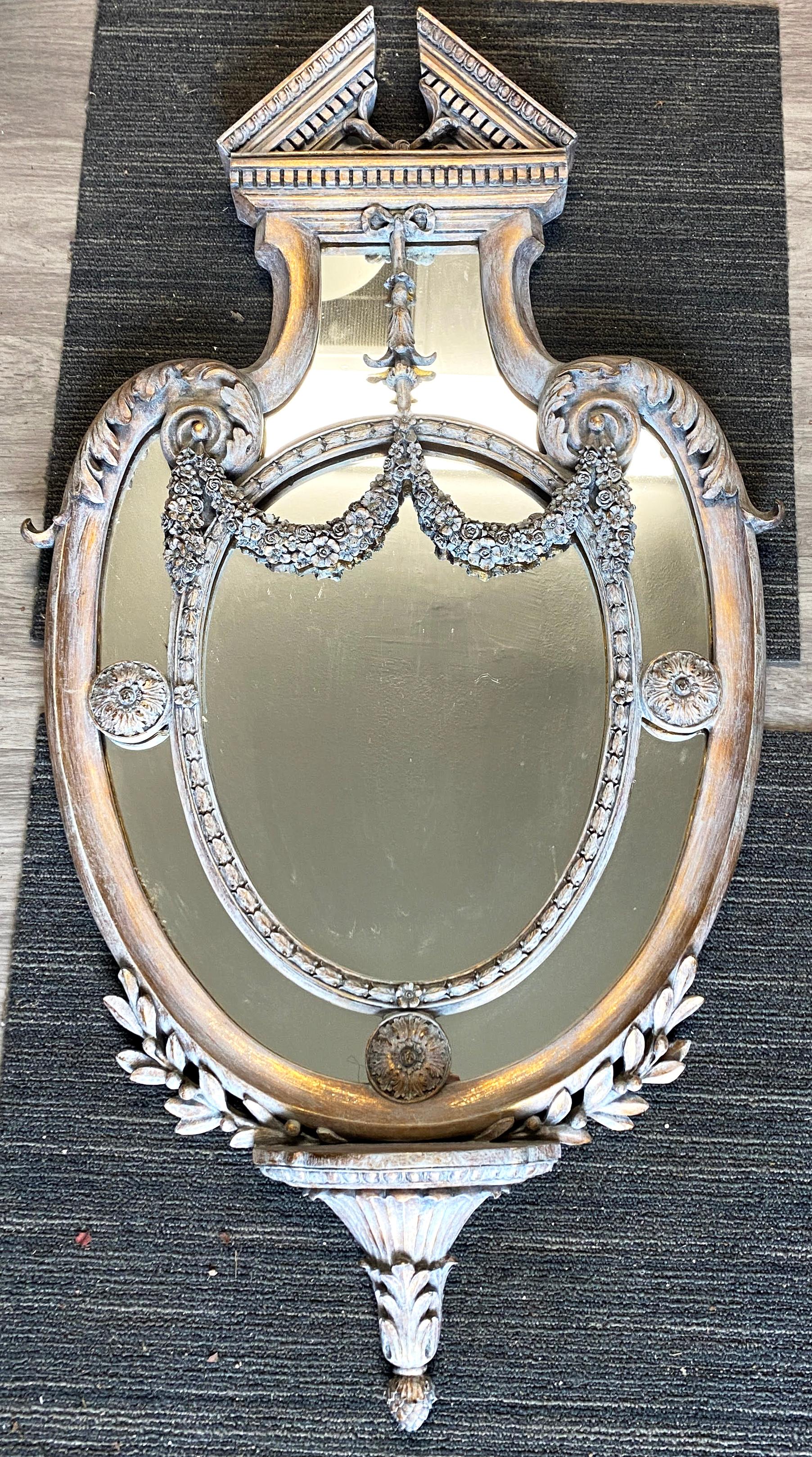 Neoclassical style gray wash painted over giltwood wall mirror, 20th c., having split pediment crest, over floral swags, shaped frame, encasing sectioned flat mirror plate, ending in foliate finial. More recently painted with gray wash by Antique