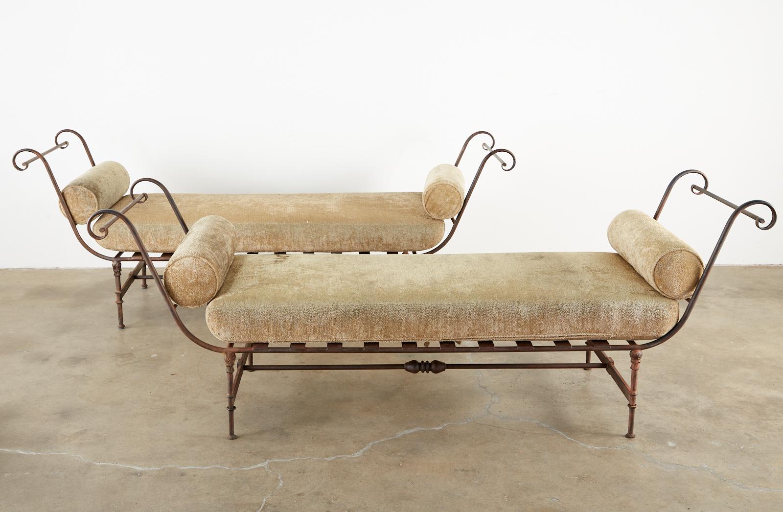 Matching pair of iron garden daybeds or benches made in the neoclassical taste. The large frames feature gracefully curved handles on each side ending with scrolls. The benches are supported by column style legs decorated with acanthus and conjoined