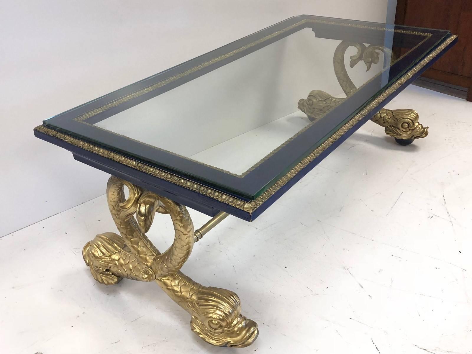 Neoclassical style carved wood dolphin coffee table. Top of the table is painted blue and the ball feet are painted blue as well. The dolphins are carved wood and the stretcher is solid brass. Nice sized glass top.