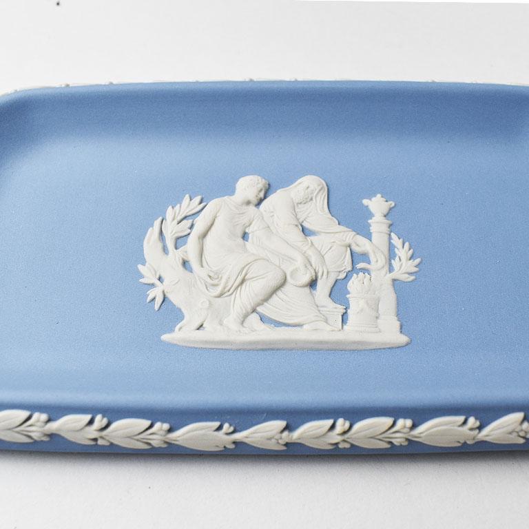 A lovely blue collectible trinket dish in matte Wedgwood blue with a neoclassical design. This piece is rectangular, with geometric sides. Applied in cream along the rim is an embossed vine of fern leaves and berries. The middle of the vide poche