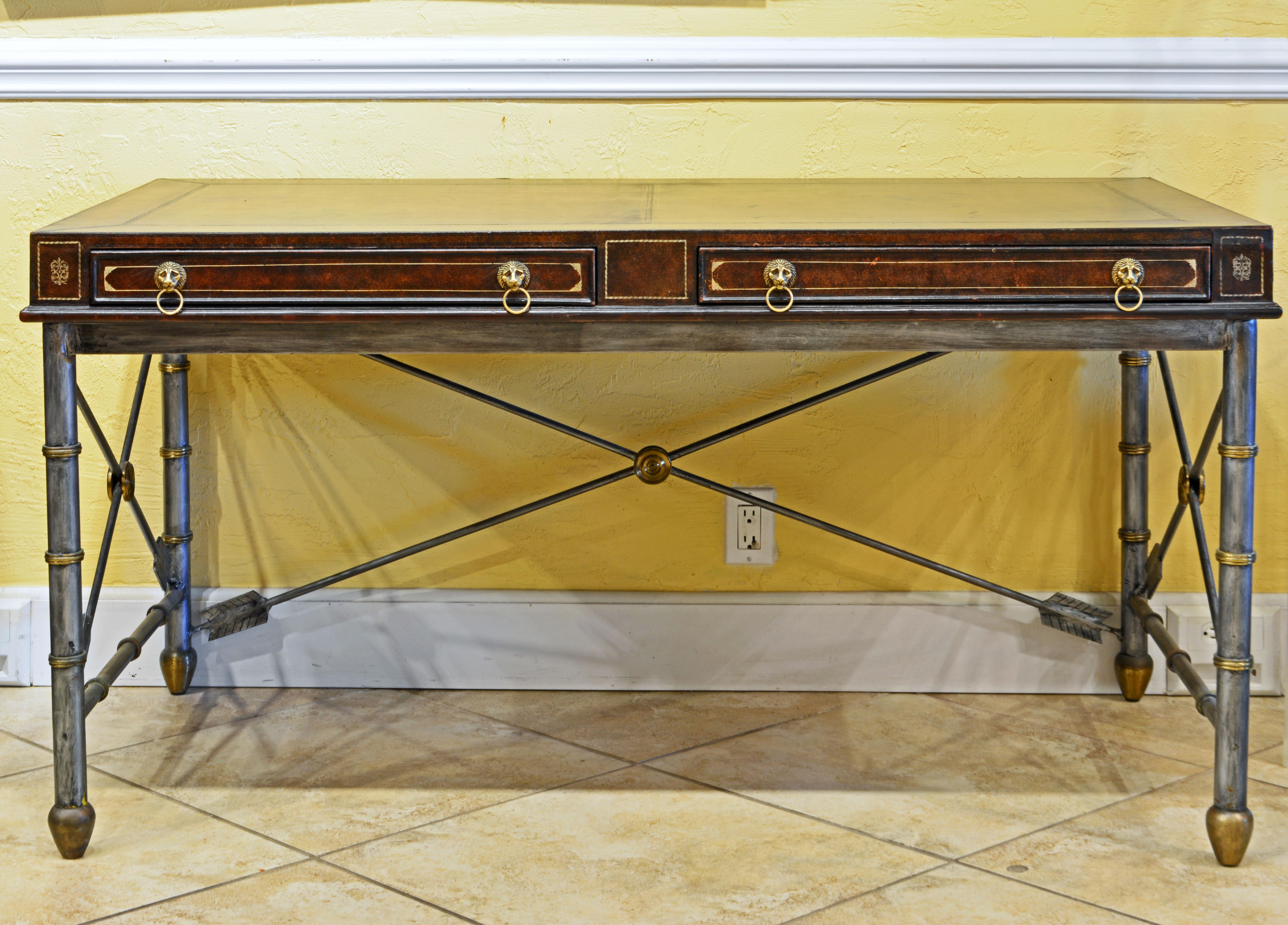 This-Maitland Smith desk or writing table features a top lined on all sides with gilt tooled leather and containing two book paper lined drawers and mounted with lion's head pulls. The neoclassical brass accented metal base rests on cone shaped