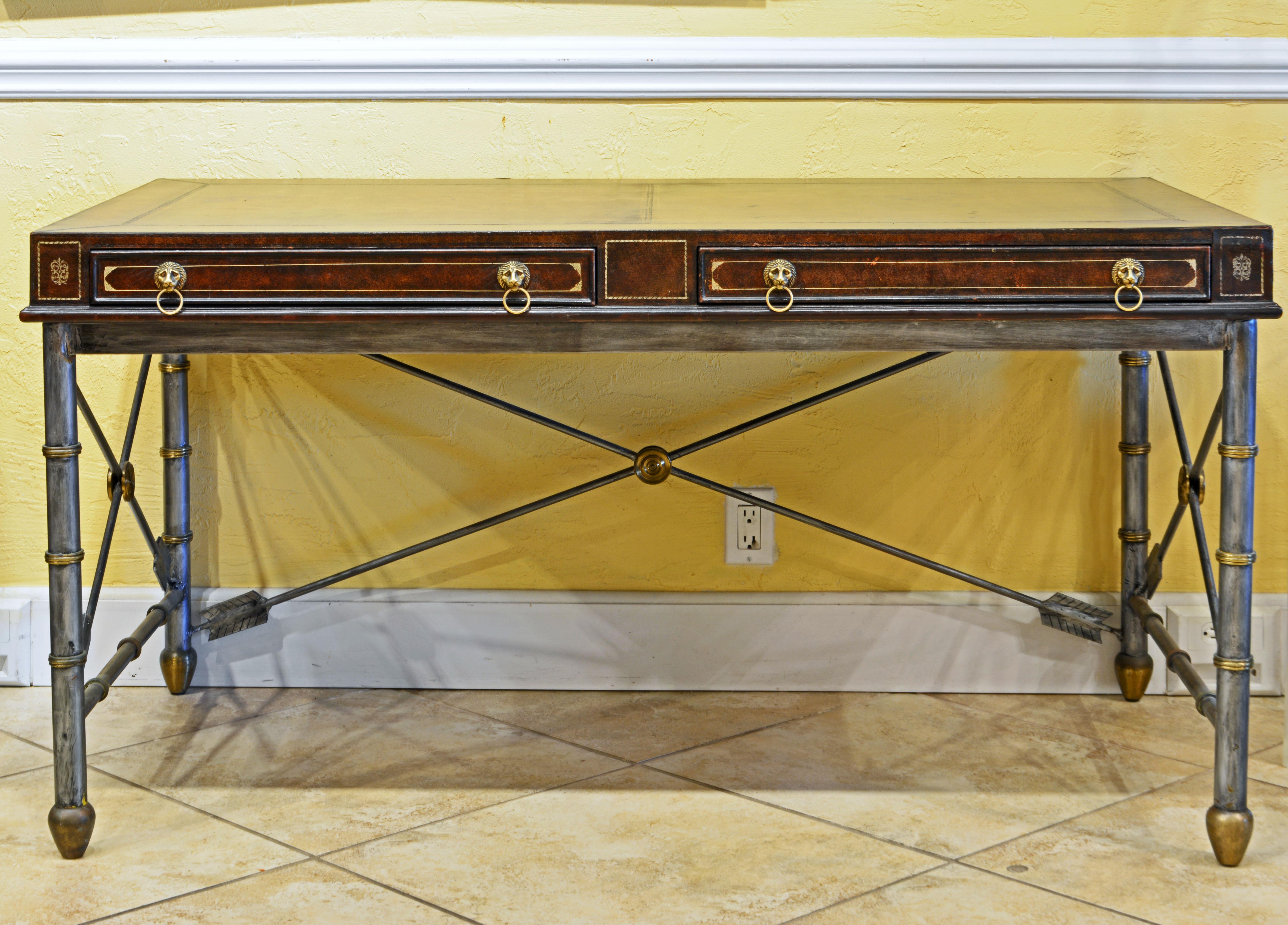 This-Maitland Smith desk or writing table features a top lined on all sides with gilt tooled leather and containing two book paper lined drawers and mounted with lion's head pulls. The neoclassical brass accented metal base rests on cone shaped