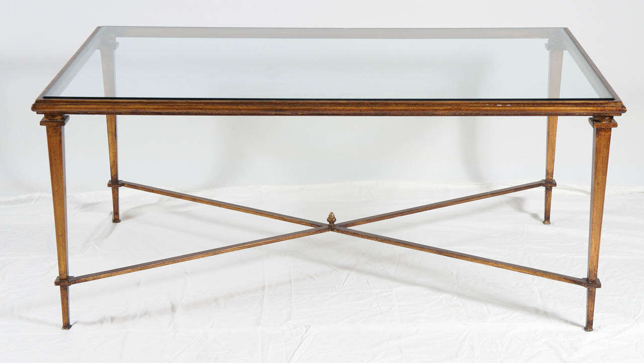 Neoclassical style bronze colored metal coffee table with cross stretcher at the base and glass top.