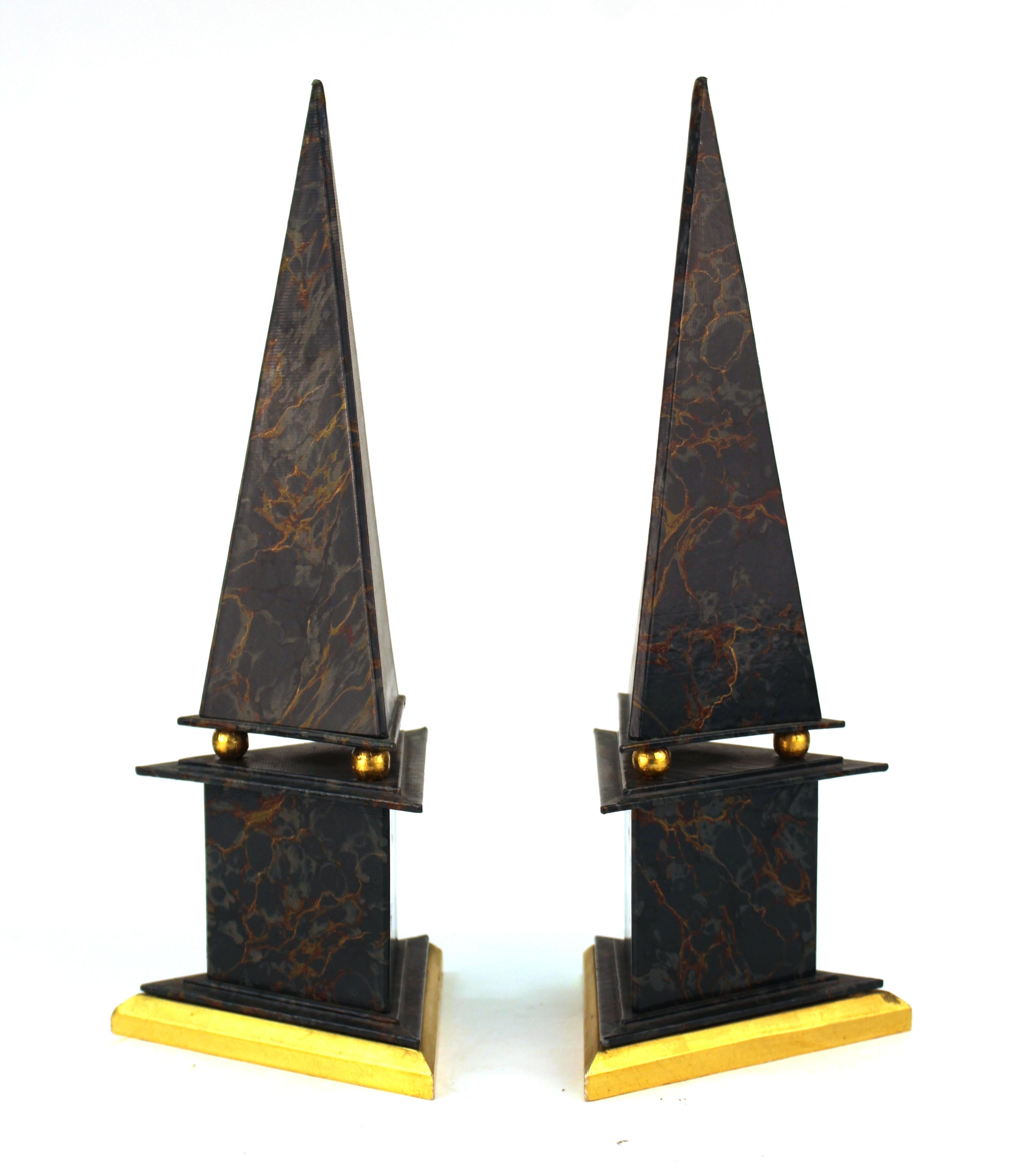 Pair of neoclassical Revival style obelisks made of cardboard with marbled paper and gold foil accents. Each obelisk is triangular shaped and rests atop a base held up by gilt spheres. In great vintage condition.