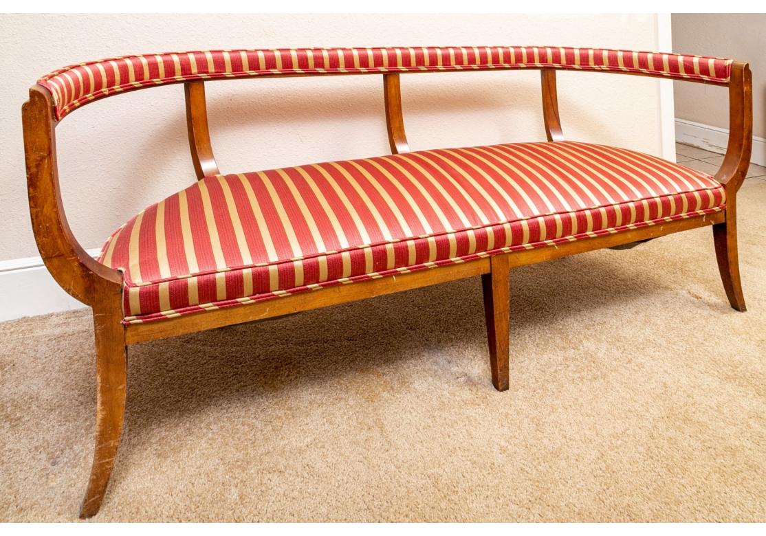 A uniquely shaped settee with a curved open wood frame and tall back to the cushioned seat.  With surprising weight and comfort and having  gold striped upholstered fabric to seat and back panel. 

Dimensions: 65
