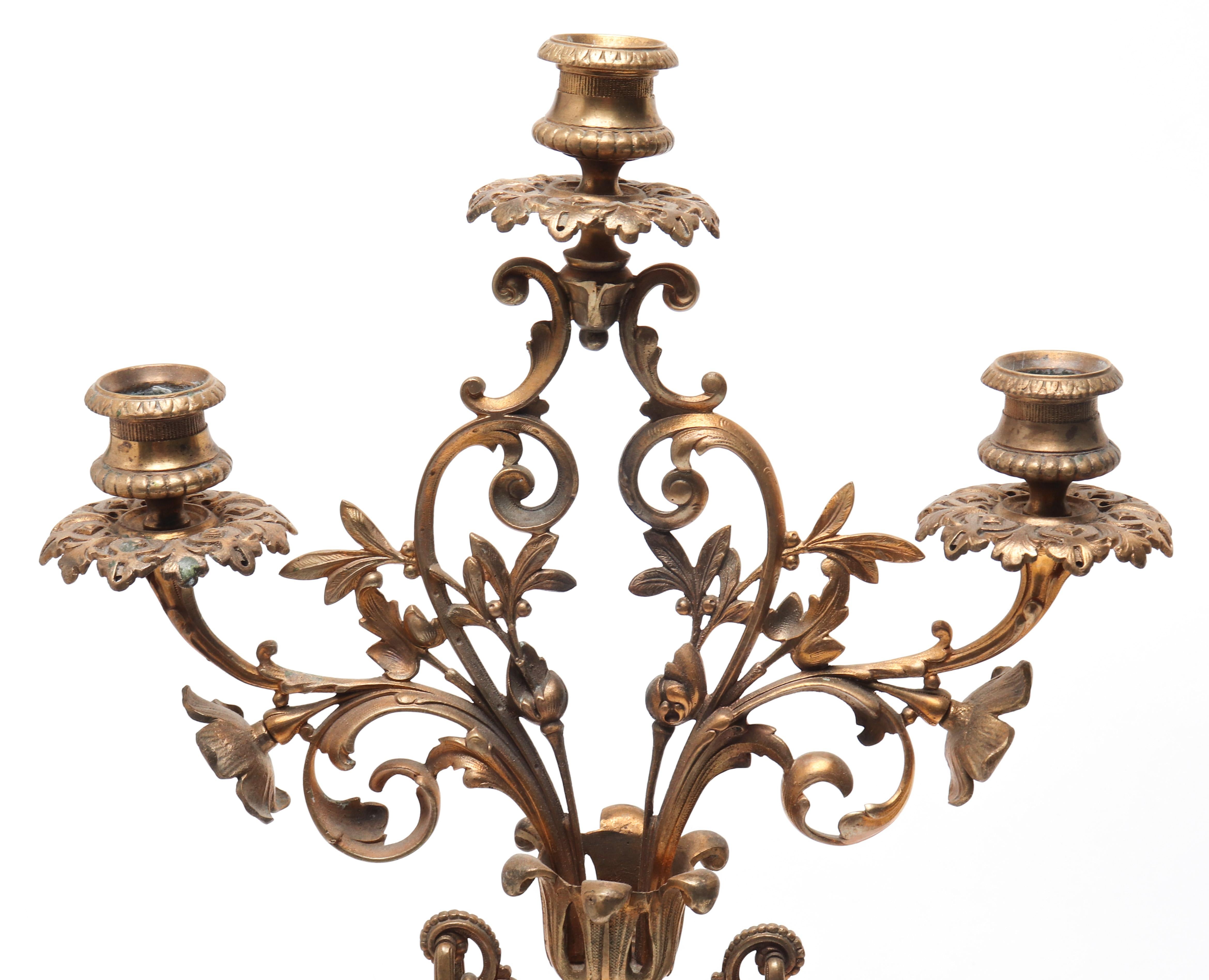 Continental pair of neoclassical style three arm candelabras with an ormolu mounted urn-form deep oxblood enamel body. The pair is topped with a bronze bouquet forming candle branches, and has three bronze feet supporting an enamel base. In great