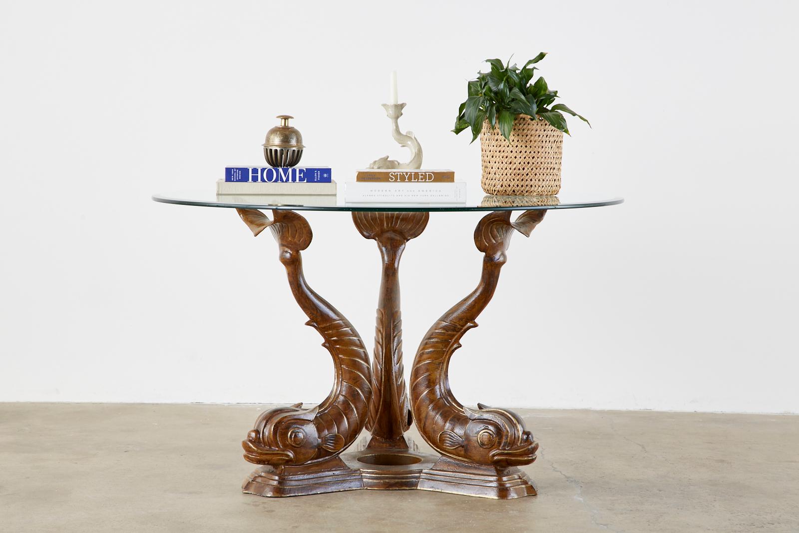 Fantastic round dining table or center table featuring a trio of stylized mythical dolphins depicted in the neoclassical taste. Surmounted by a round pane of beveled glass. The dolphins are mounted to a stepped base and have a hand painted parcel