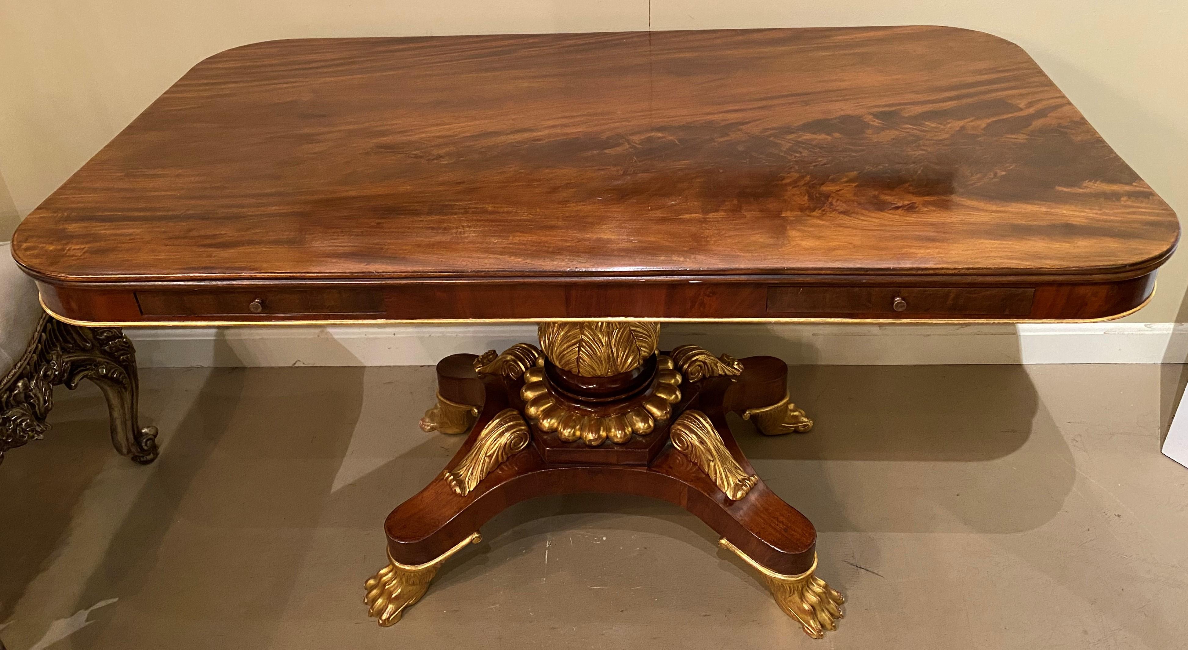 A beautiful example of a neoclassical style rectangle parcel gilt carved mahogany library, writing or center table with figured mahogany veneer top with rounded corners, two small document frieze drawers, acanthus and scroll carved center pedestal,