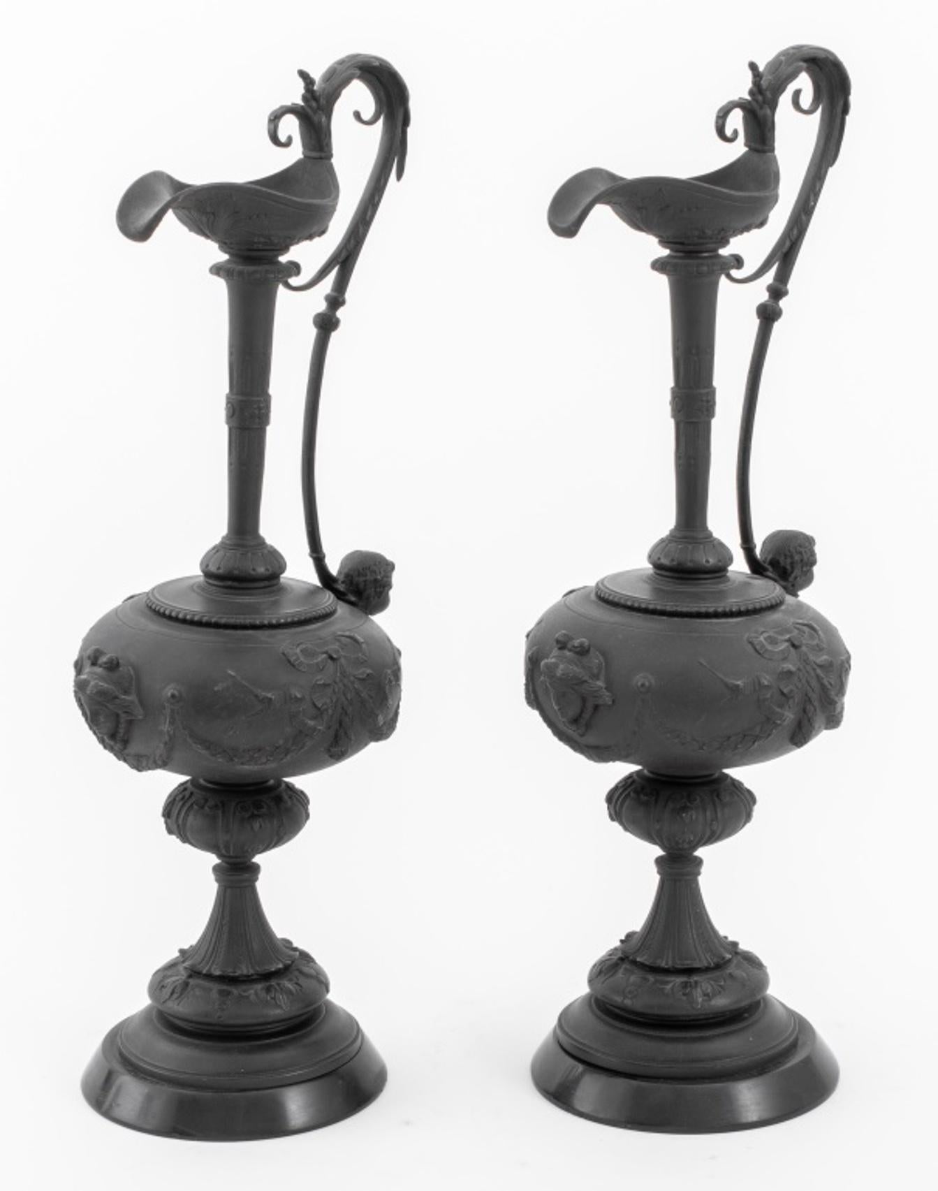 Pair of patinated bronze ewer form sculptures cast with Neoclassical manner decoration of foliate accents, bows, busts of putti below handles, and masques to front, mounted upon black marble stone bases.

Dimensions: Each: 18.75