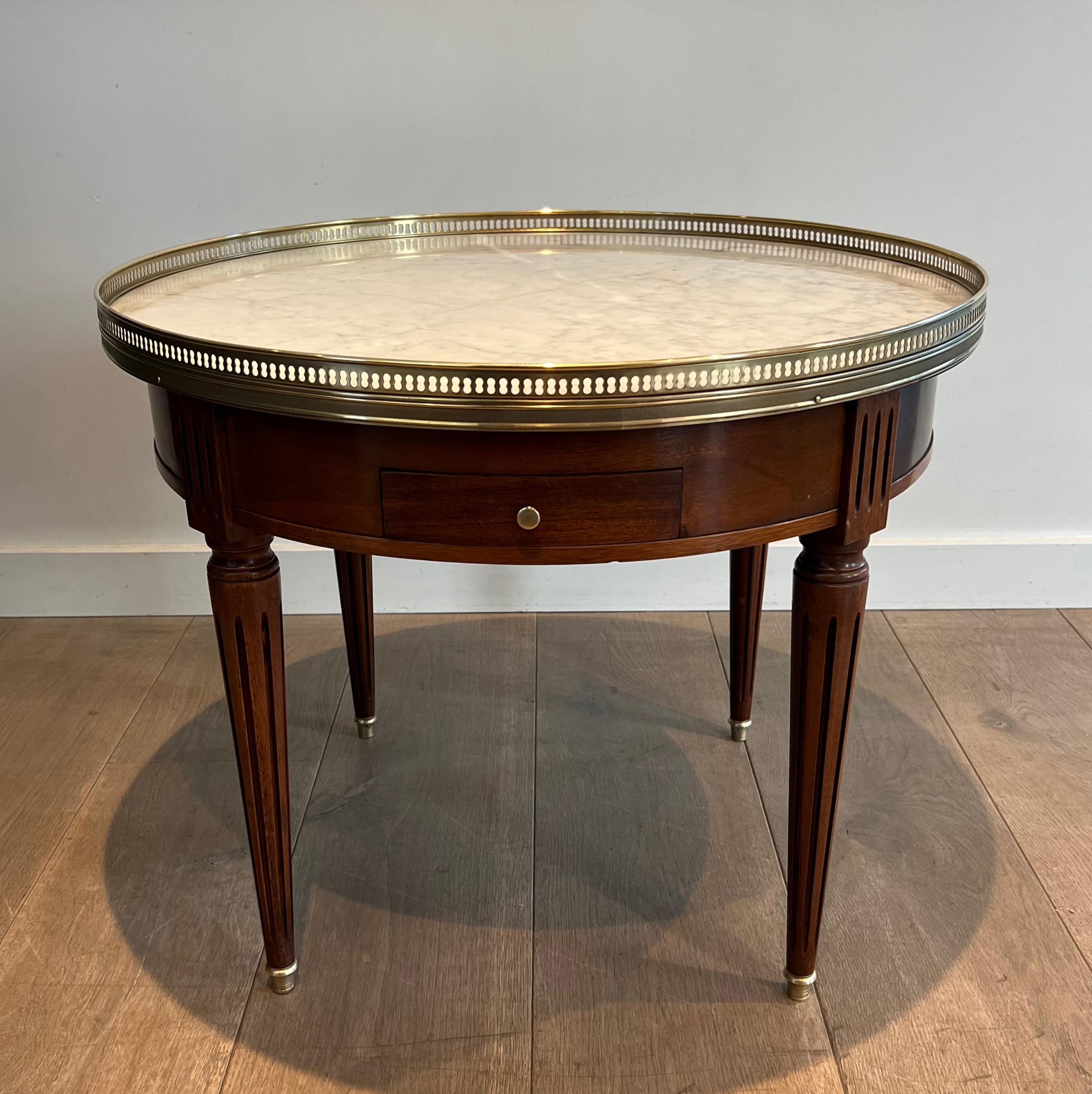 This neoclassical style round coffee table is made of mahogany with Carrara marble top surrounded by an openwork brass gallery. The pedestal table has 2 drawers and 2 leather-trimmed pulls. This is a French work in the style of famous designer