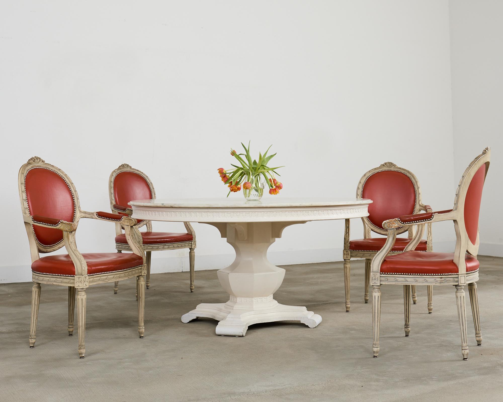 Imposing round pedestal center table or dining table featuring a thick Carrara marble top. The large table has a decorative frieze with a scrolled quatrefoil design around the edge. The top is supported by a substantial urn form having a stepped