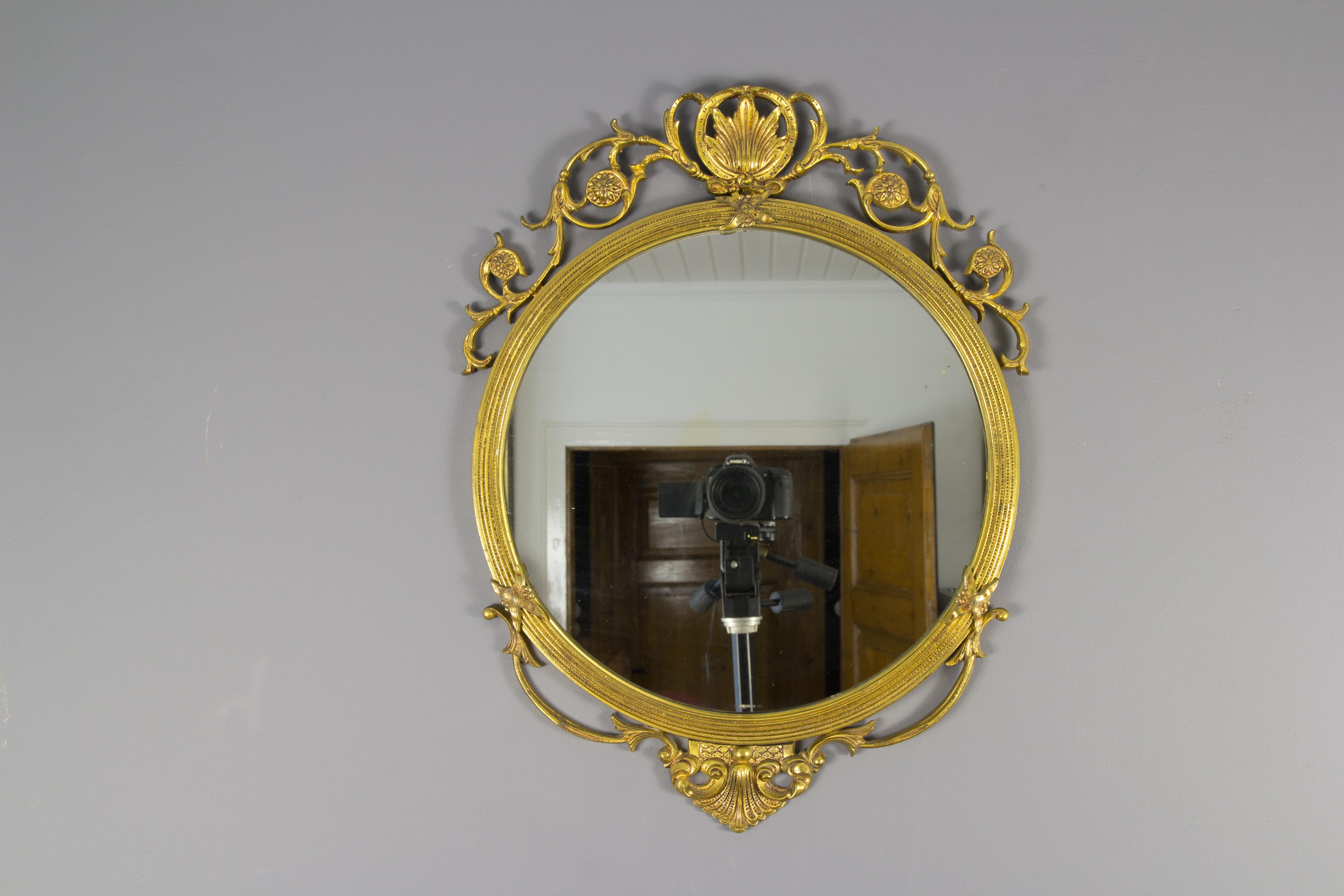 Neoclassical style round wall mirror, bronze frame decorated with rosettes, scrolls and foliate details. France, circa 1930s.
Dimensions: height: 58 cm / 22.83 in; width: 45 cm / 17.71 in; depth: 2.5 cm / 0.98 in.
     