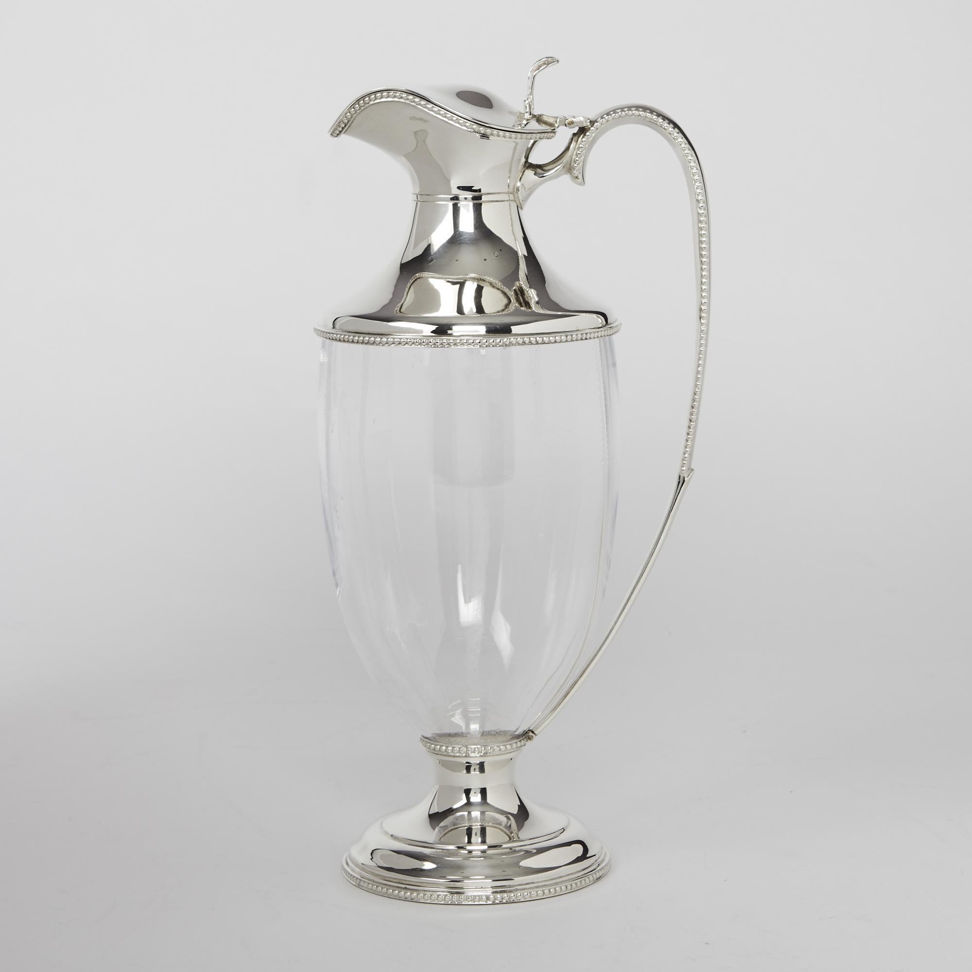 Modern recreation of a neoclassical, Adam-style wine jug with glass body and silver mounts decorated with bead patterns and with a cover featuring an elegant pierced thumbpiece. The plain hand-blown glass body tapers towards a round bead-mounted