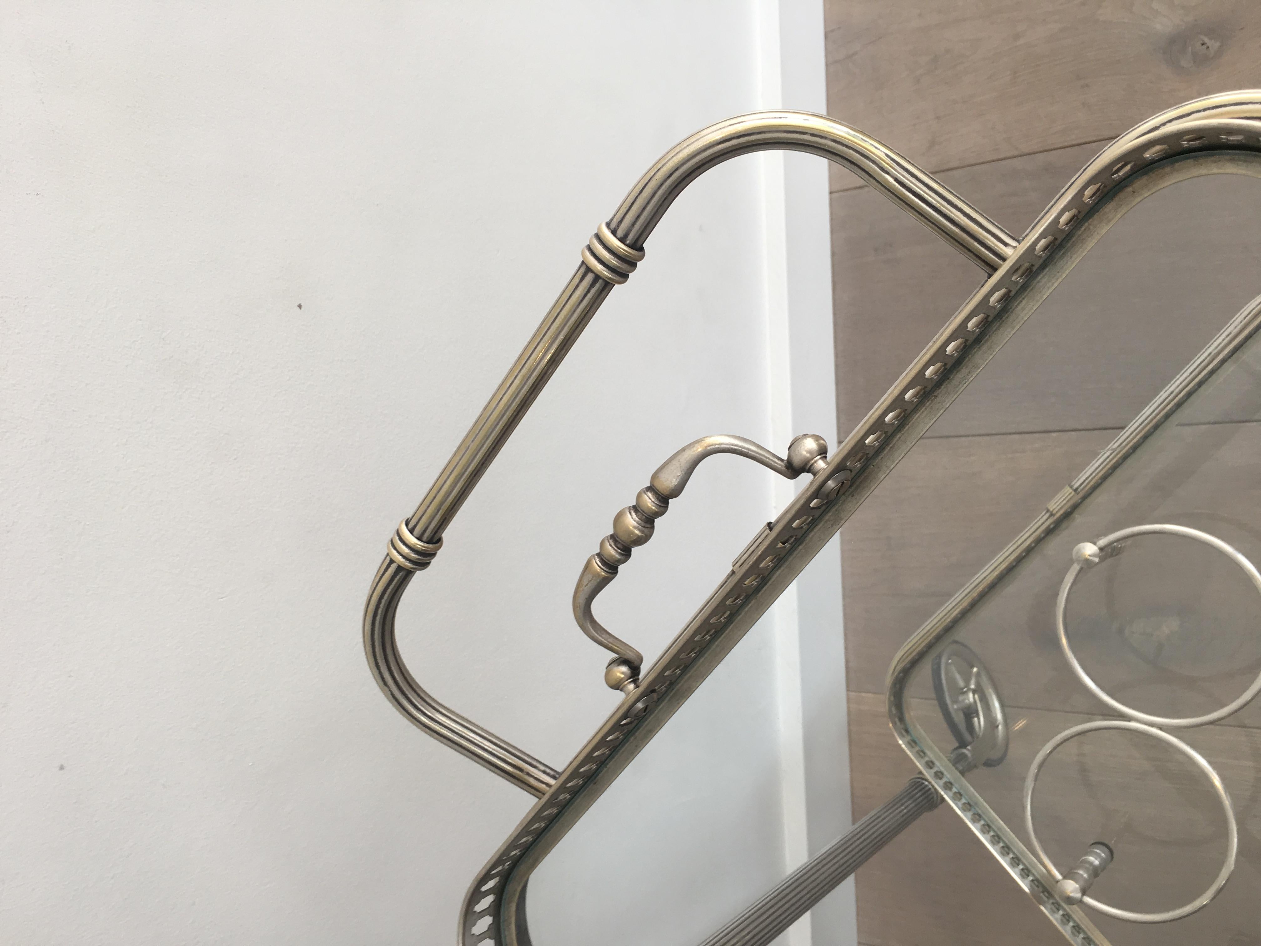 French 1940s Neoclassical style bar cart with silvered brass finish. Features a removable glass top serving tray and bottle rack on bottom shelf.