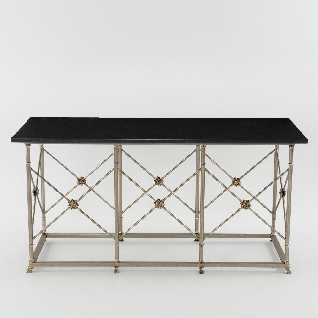 20th Century Jansen style console. Each oversized stately table features polished steel, brass rosettes and lions paw feet supporting a black granite top. Two available, sold individually.