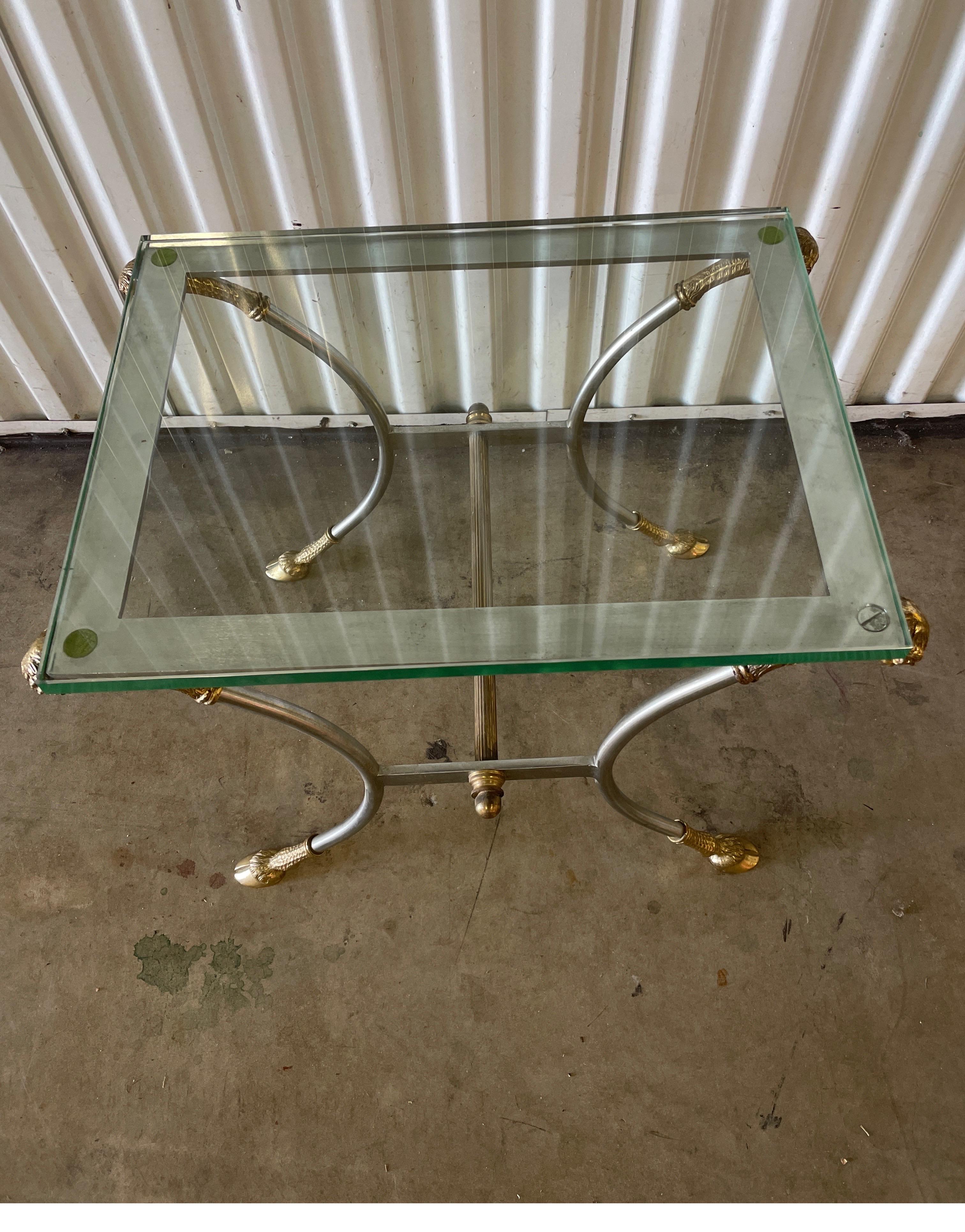 Vintage Neoclassical Ram's Head and Hoof side table by Jansen. This polished steel & brass table has a thick glass top. Perfect little drinks table.
A classic gem.