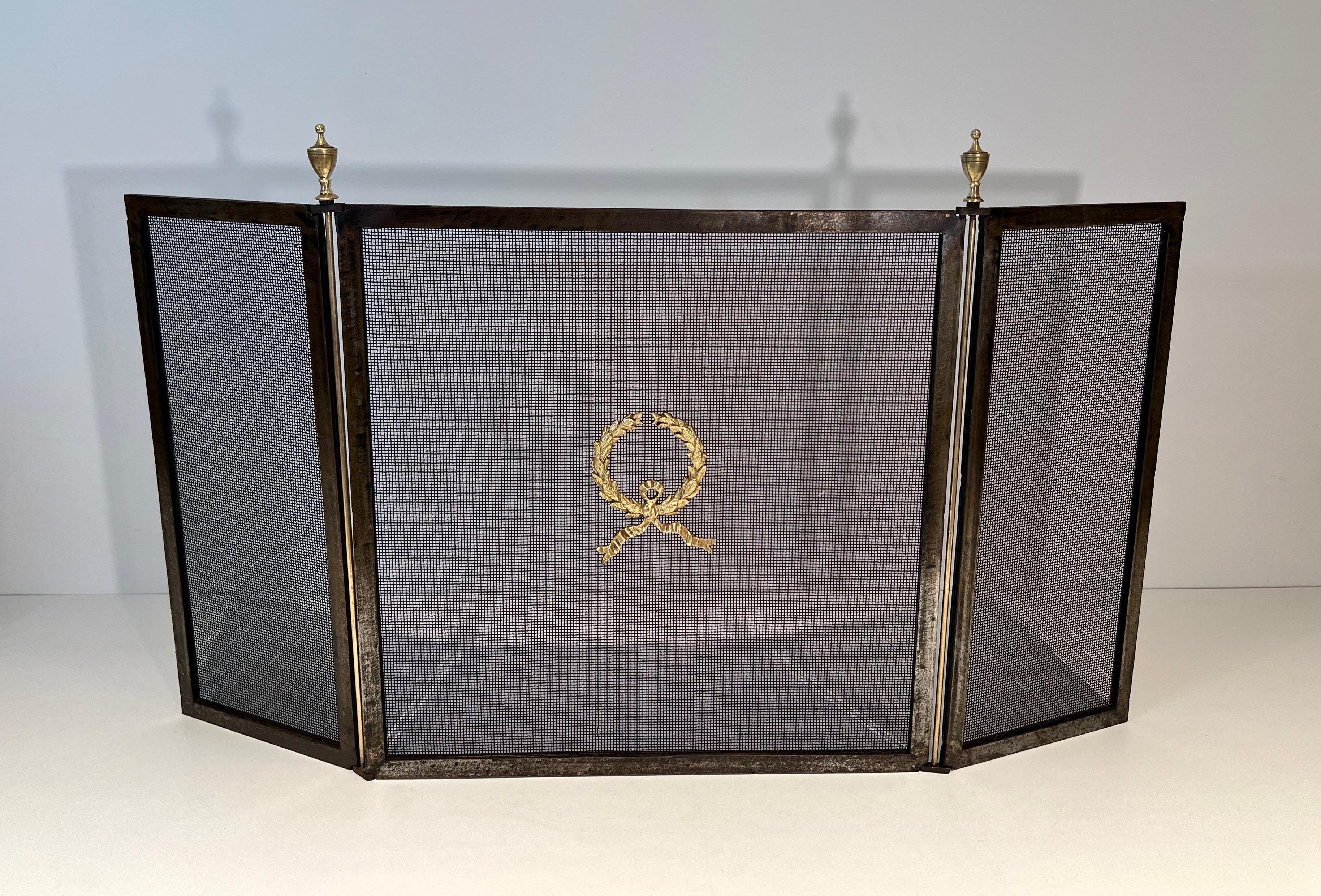 This neoclassical style fireplace screen with 3 panels is made of steel and brass with a grilling on each panel. The central part is decorated with a laurel wreath. This is a French work. Circa 1940