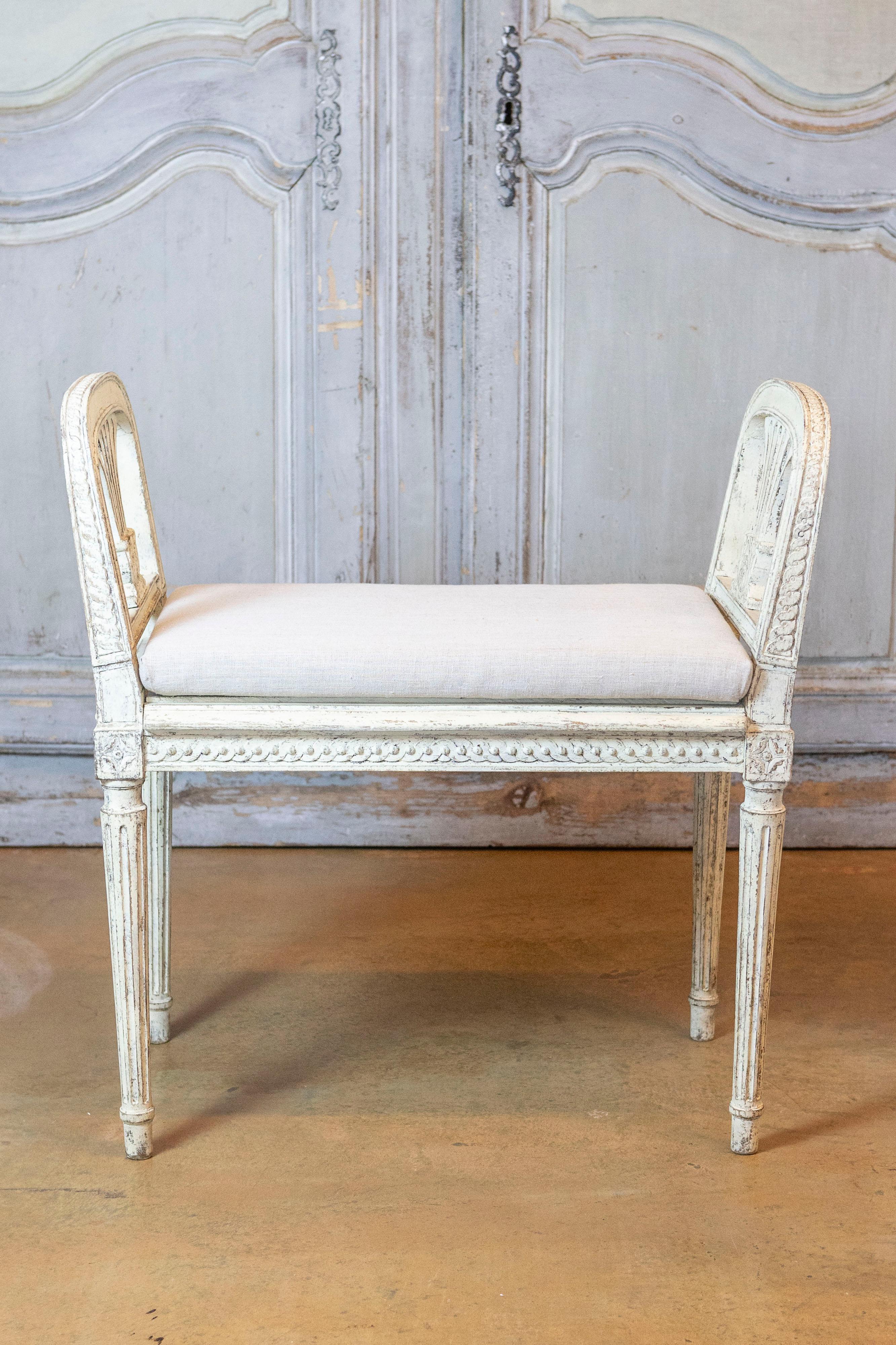 A Swedish Neoclassical style small bench from the 20th century with gray and cream painted finish, carved side supports, guilloche friezes and fluted legs. This Swedish Neoclassical style small bench, crafted in the 20th century, is a stunning
