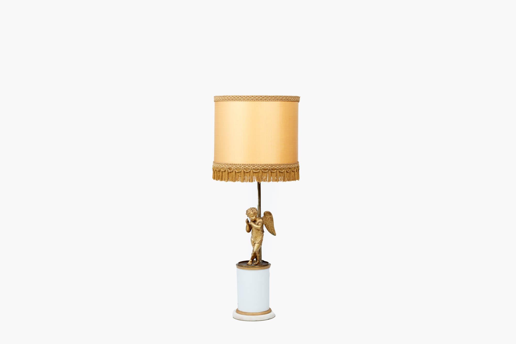 Tischlampe des frühen 20. Jahrhunderts im neoklassizistischen Stil mit geflügelter Puttenfigur über einem schweren, weißen, zylindrischen Säulensockel mit vergoldeten Bändern an Kopf und Fuß.
