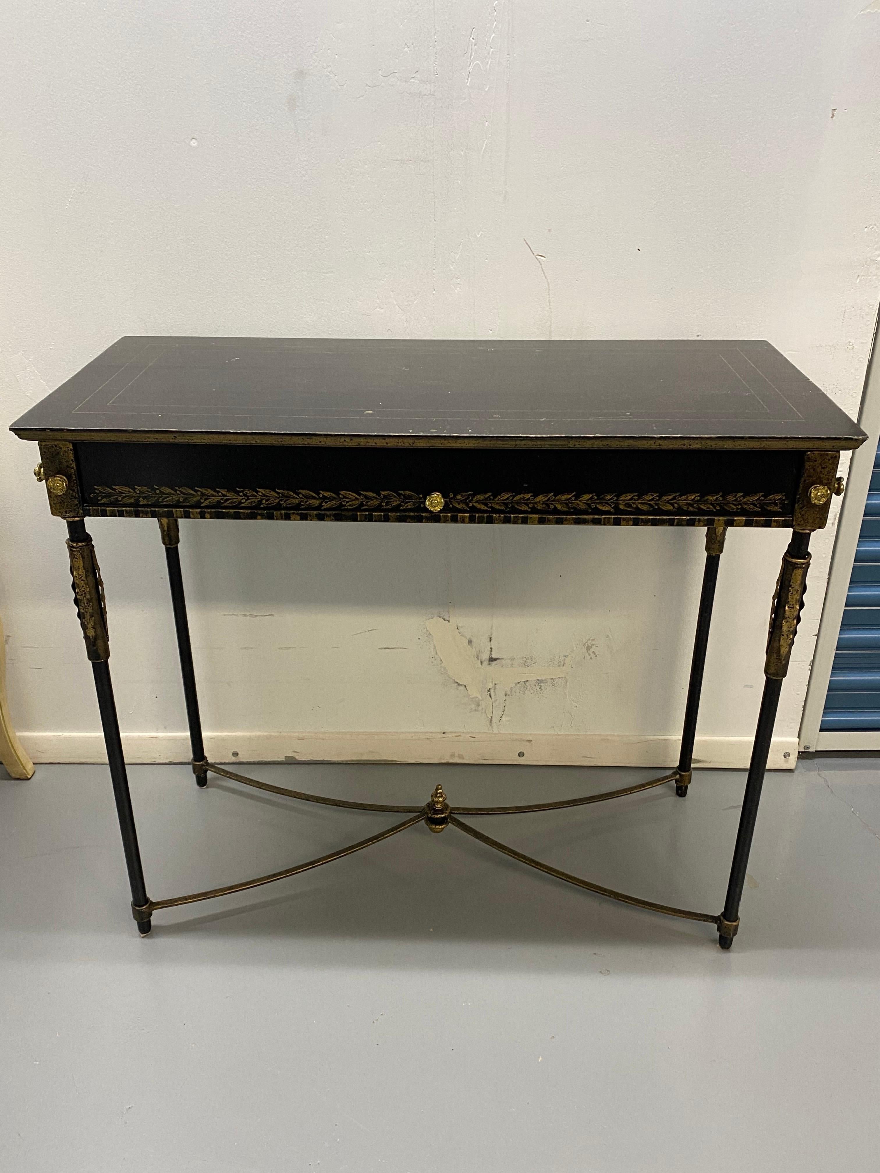 Neoclassical Style Table with Painted Decoration by Art & Commerce
Ebonized wood frame with metal stretcher and brass detailing. Speckled faux finish on top with gold painted leaf decoration on front rail, pin stripe banding on top. Brass finials on
