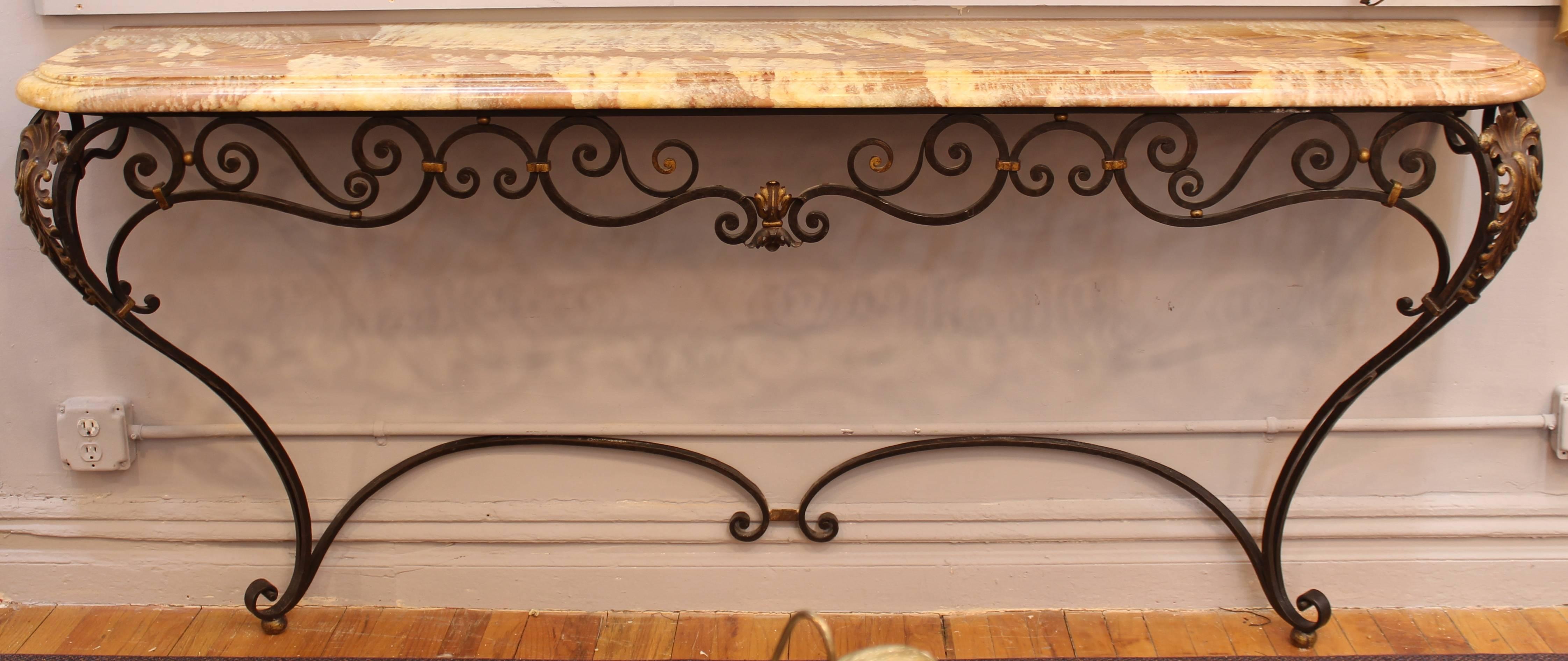 A neoclassical style sideboard made of a wrought iron base with gold accents, with a shaped marble-top in shades of brown and rose. The piece is in good condition, with a large scratch on the upper left side of the marble-top.