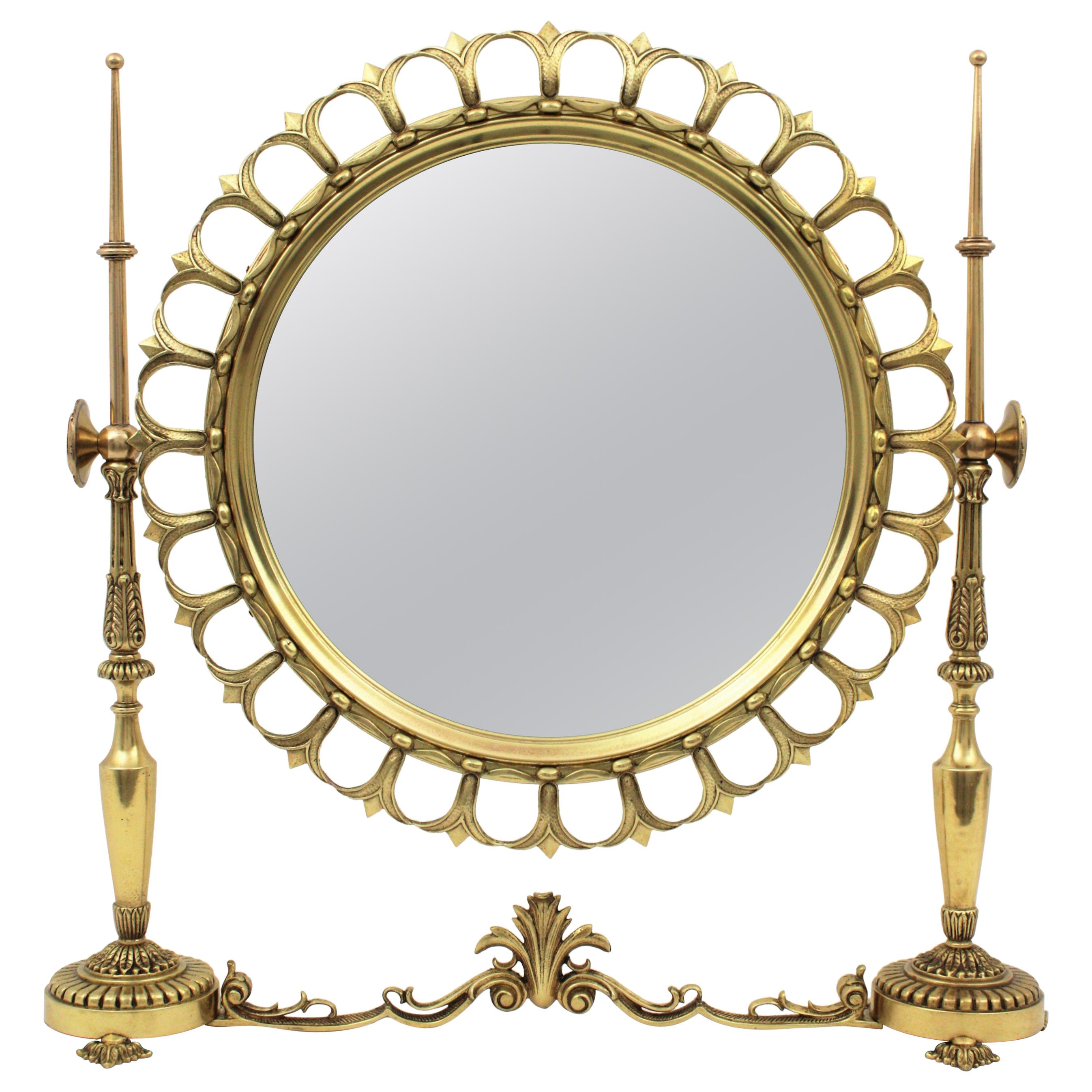 Luxury neoclassical style brass vanity tabletop swinging sunburst mirror, Spain, 1950s.
It has a fleur-de-lis pattern surrounding a round glass and classical figures finials al the sides. The round mirror is set in a brass bezel that tilts and