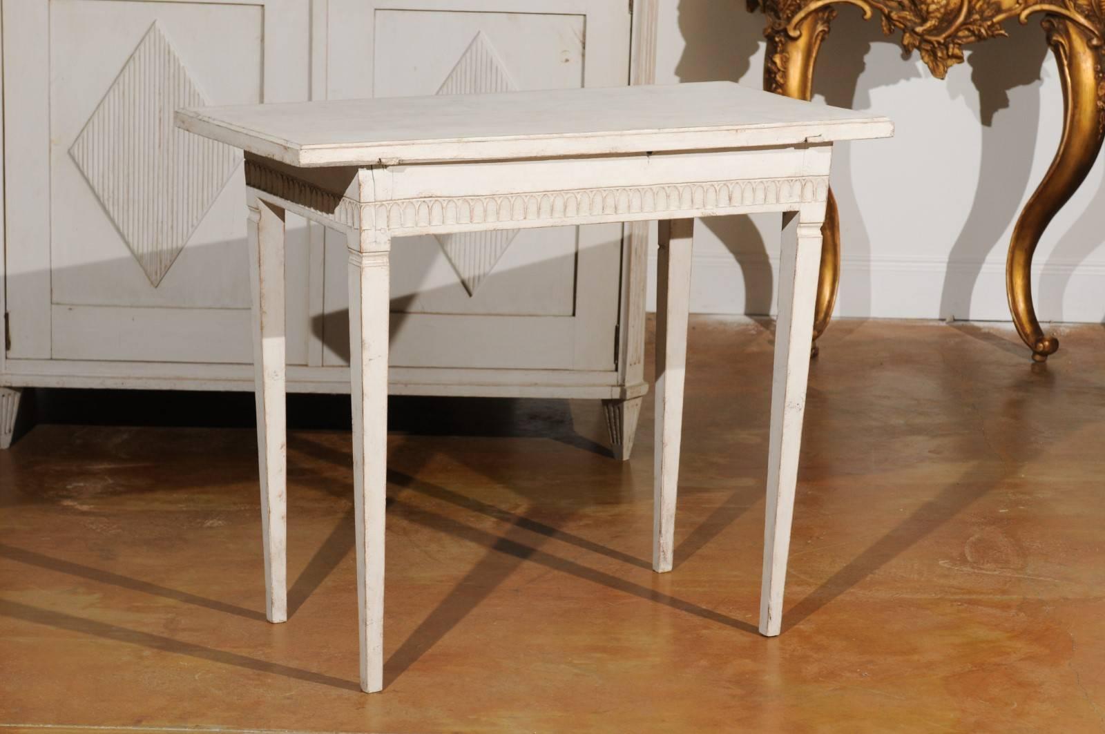 A Swedish neoclassical painted side table from the first half of the 19th century, with carved apron and tapered legs. This Swedish painted side table features a rectangular top with slightly bevelled edges, sitting above an exquisite carved apron