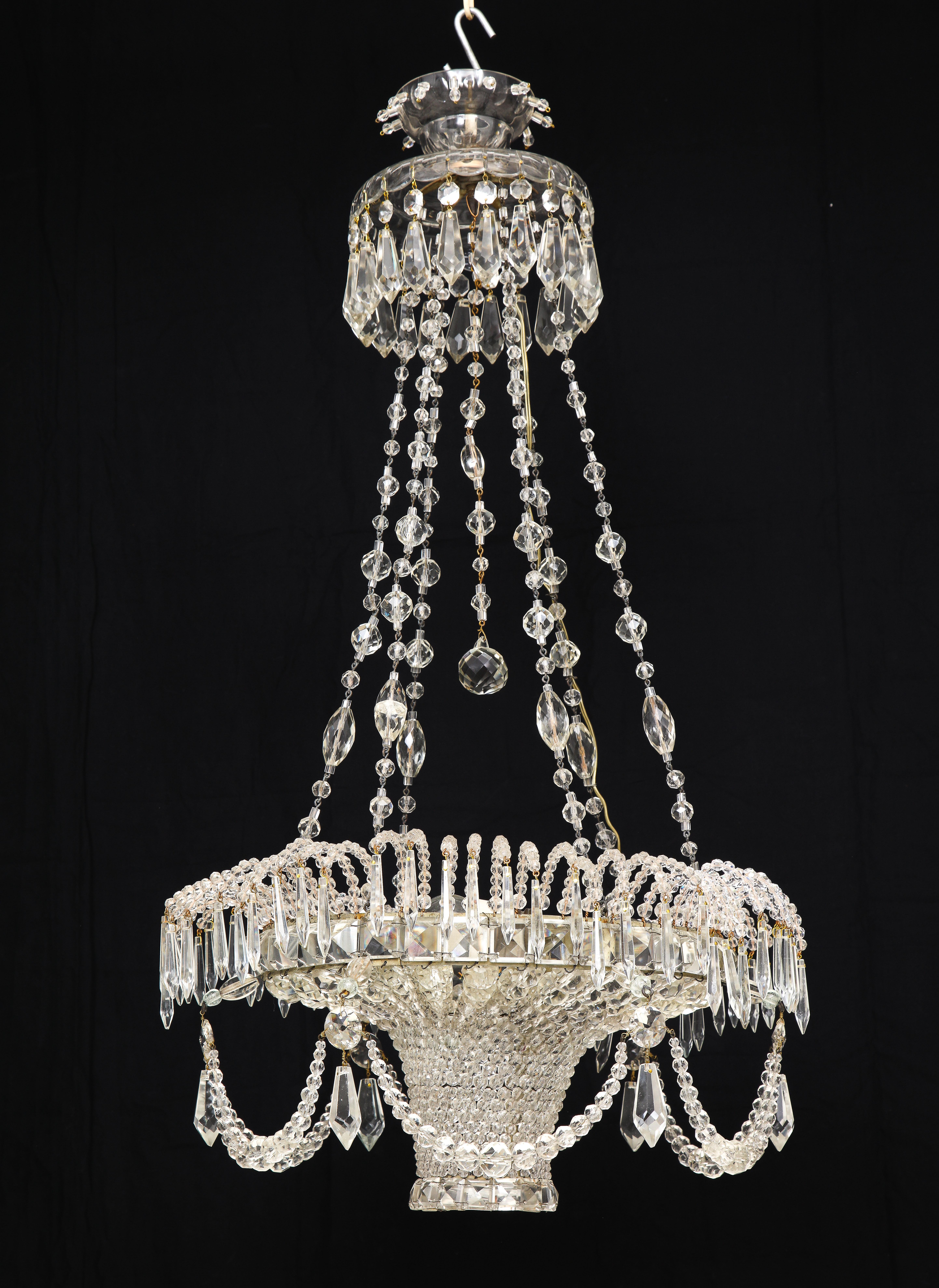 Of elegant basket form festooned with crystal garlands and hanging from a chains beaded with varying sized crystal beads, set below a cut glass collar hung with cut crystal pendants. With three-light - electrified.